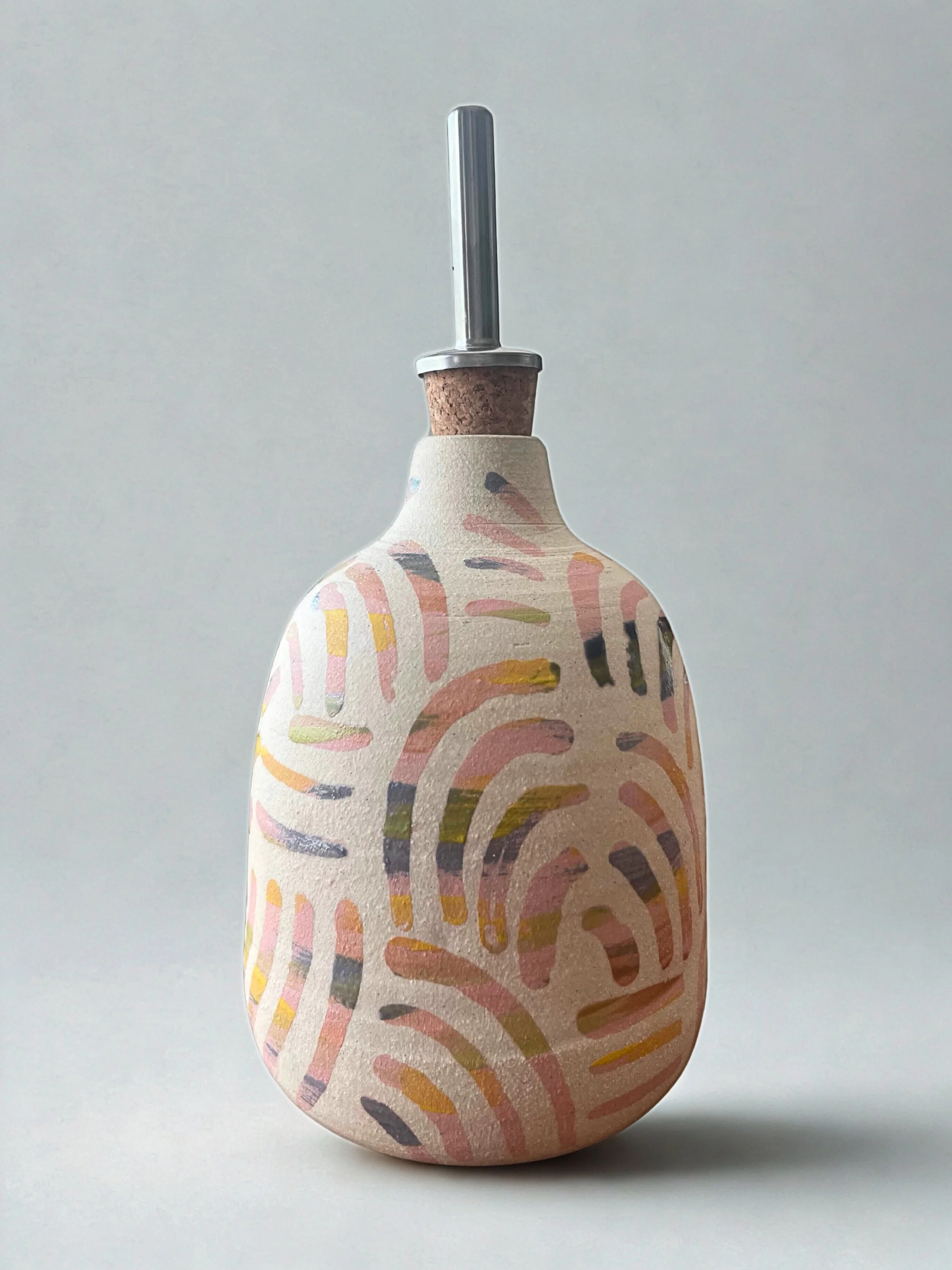 Decorative soap dispenser with a colorful, abstract, painted design, topped with a metal pump and a cork stopper, against a plain white background.