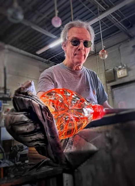 Mort Silverman, a Glassblower wearing dark protective eyewear working with hot glass in a workshop.