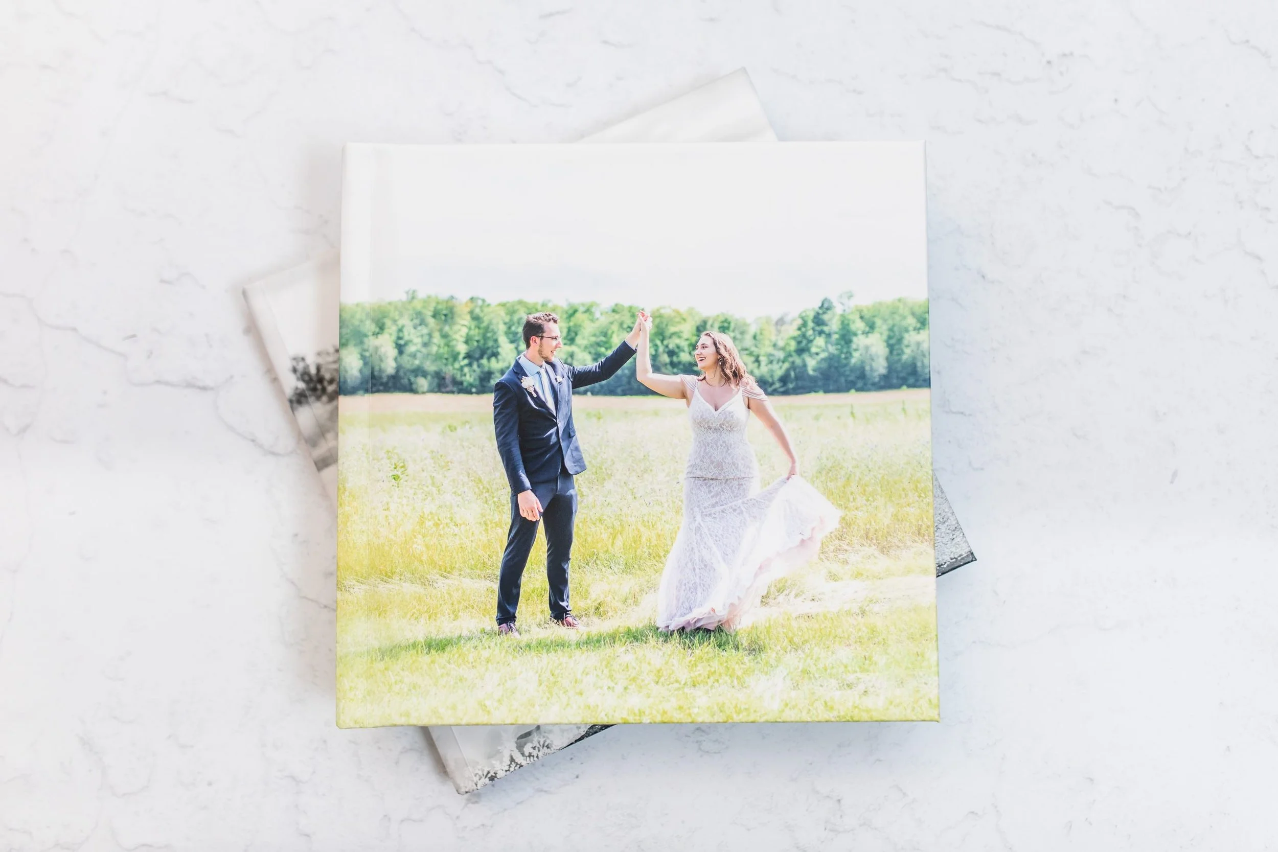 Photograph of a bride and groom dancing in a field on their wedding day, with the groom in a dark suit and the bride in a white lace wedding dress.