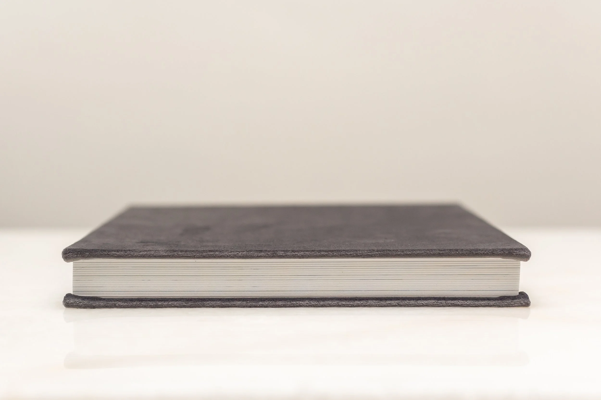 Close-up of a black hardcover book with white pages on a white surface with a neutral background.