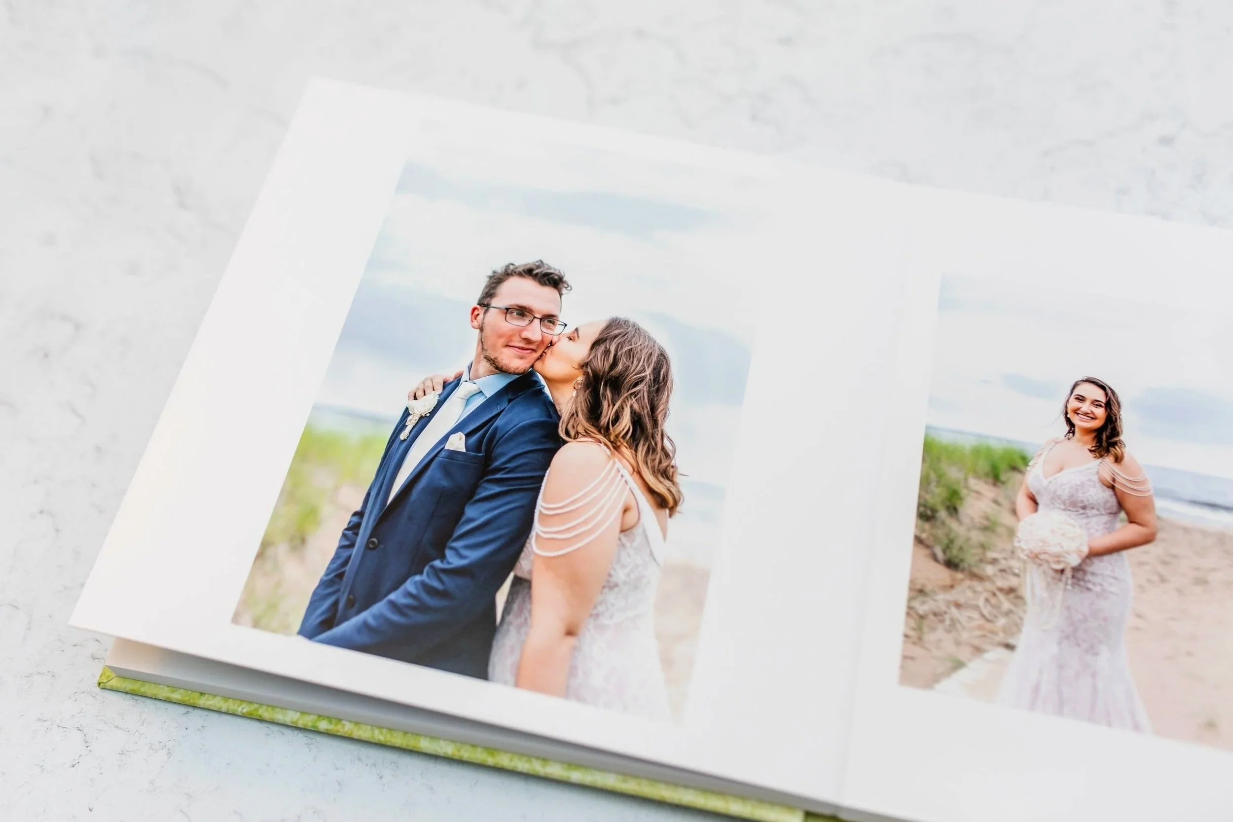 Open photo album showing wedding pictures on a beach, featuring a bride and groom and the bride standing alone, smiling.