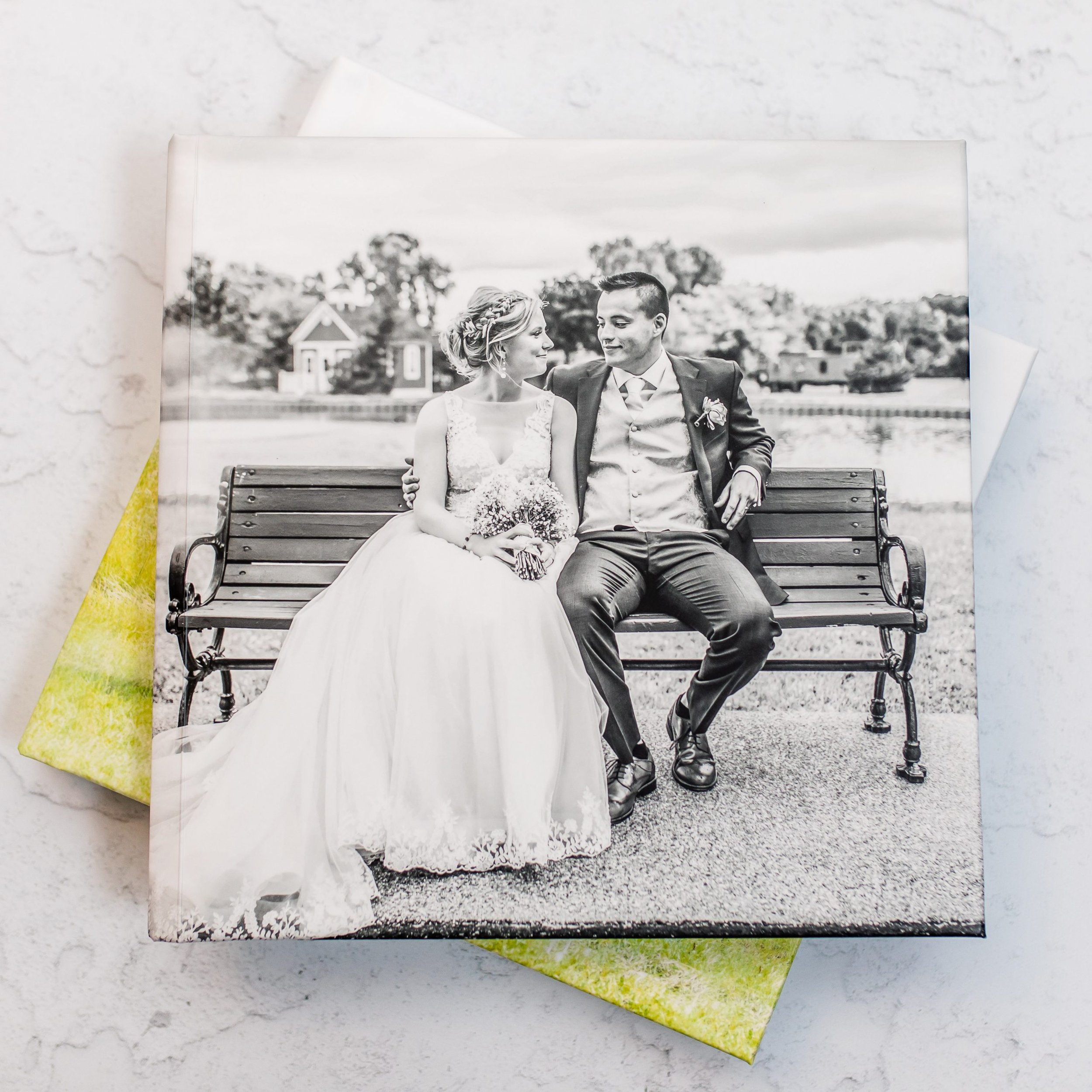 Black-and-white photo of a bride and groom sitting on a park bench, gazing at each other, with trees and a small building in the background