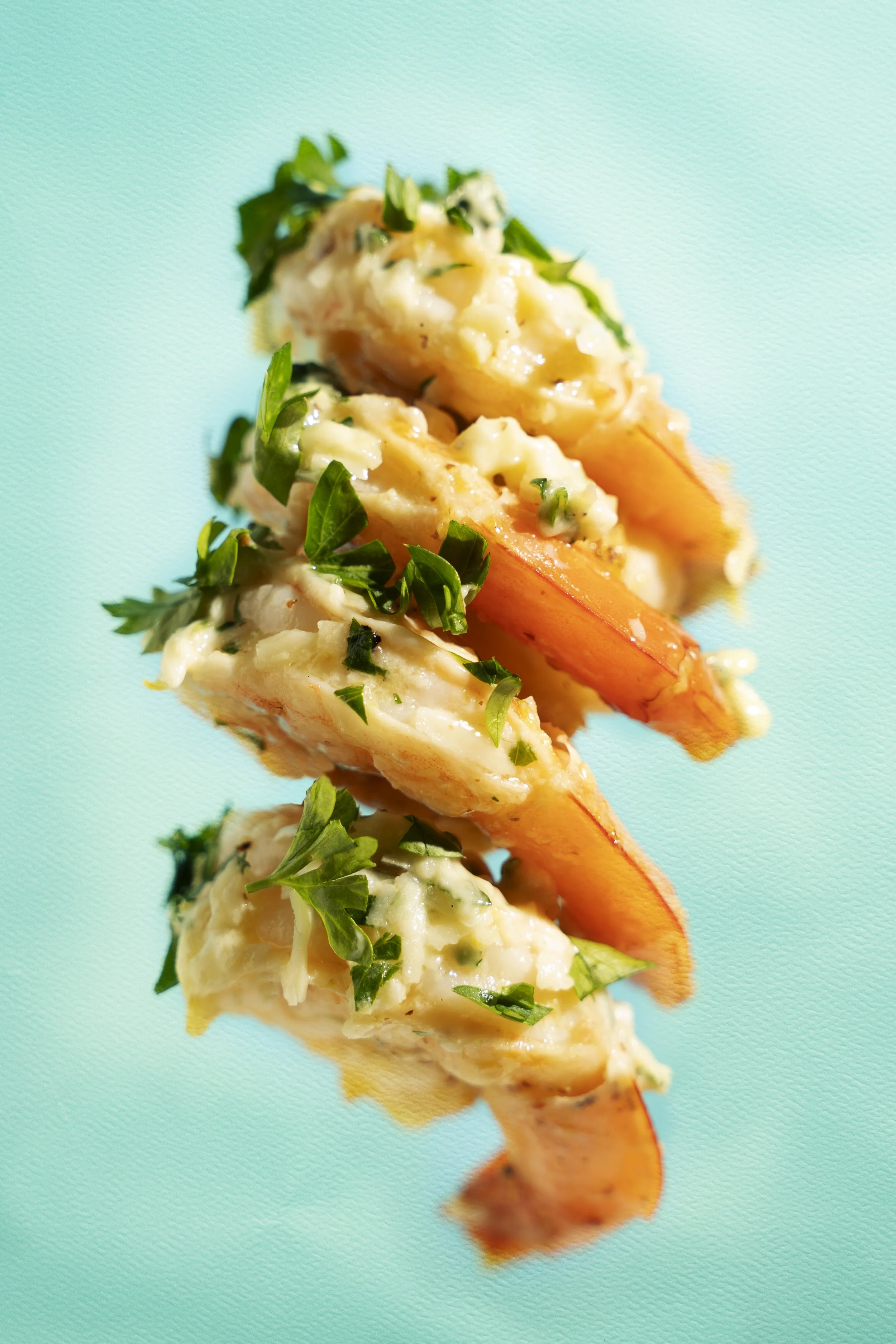 Close-up of a skewer with cooked shrimp, garnished with chopped herbs, against a turquoise background.
