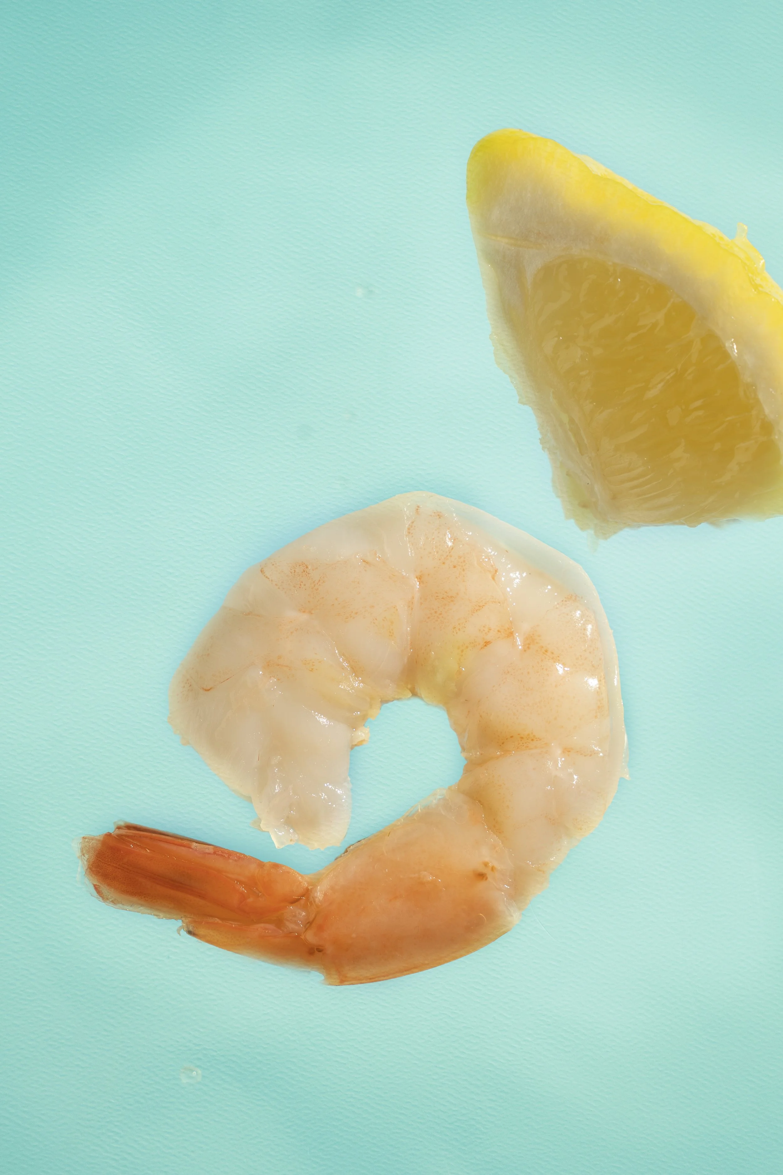 Close-up of a peeled shrimp and a lemon wedge on a turquoise background.