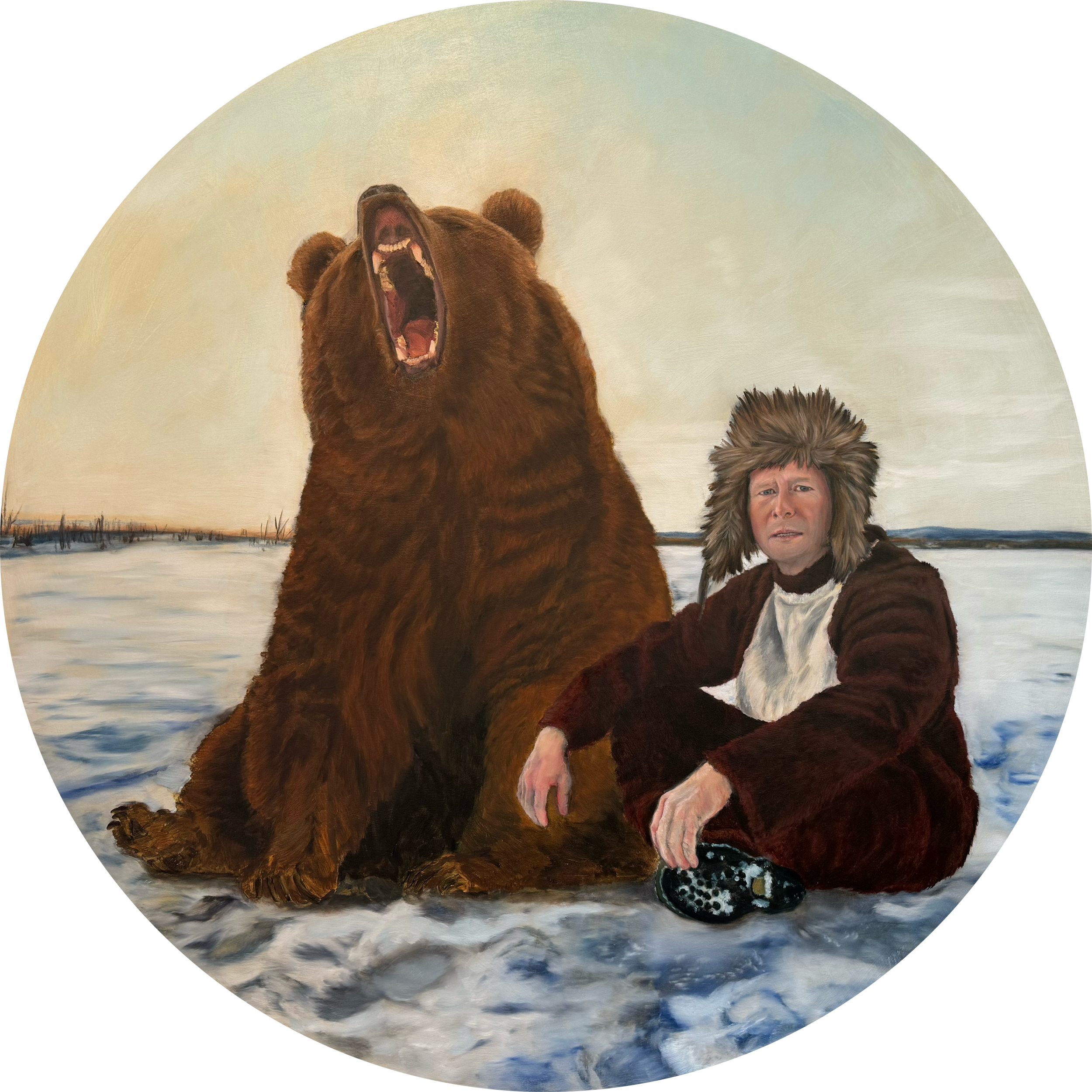 Tyler Cope wearing a horse suit and winter boots sits on snow next to a large roaring brown bear in an outdoor, winter landscape.