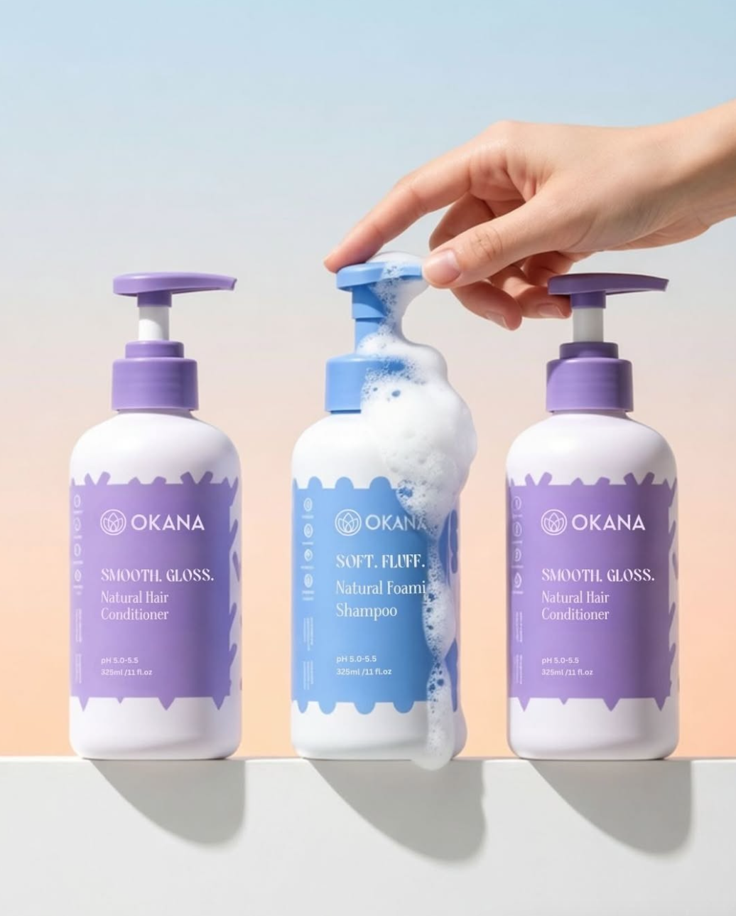 Three bottles of hair care products, two purple labeled conditioner bottles and one blue labeled shampoo bottle, with soap foam on the shampoo and a hand pressing the pump.