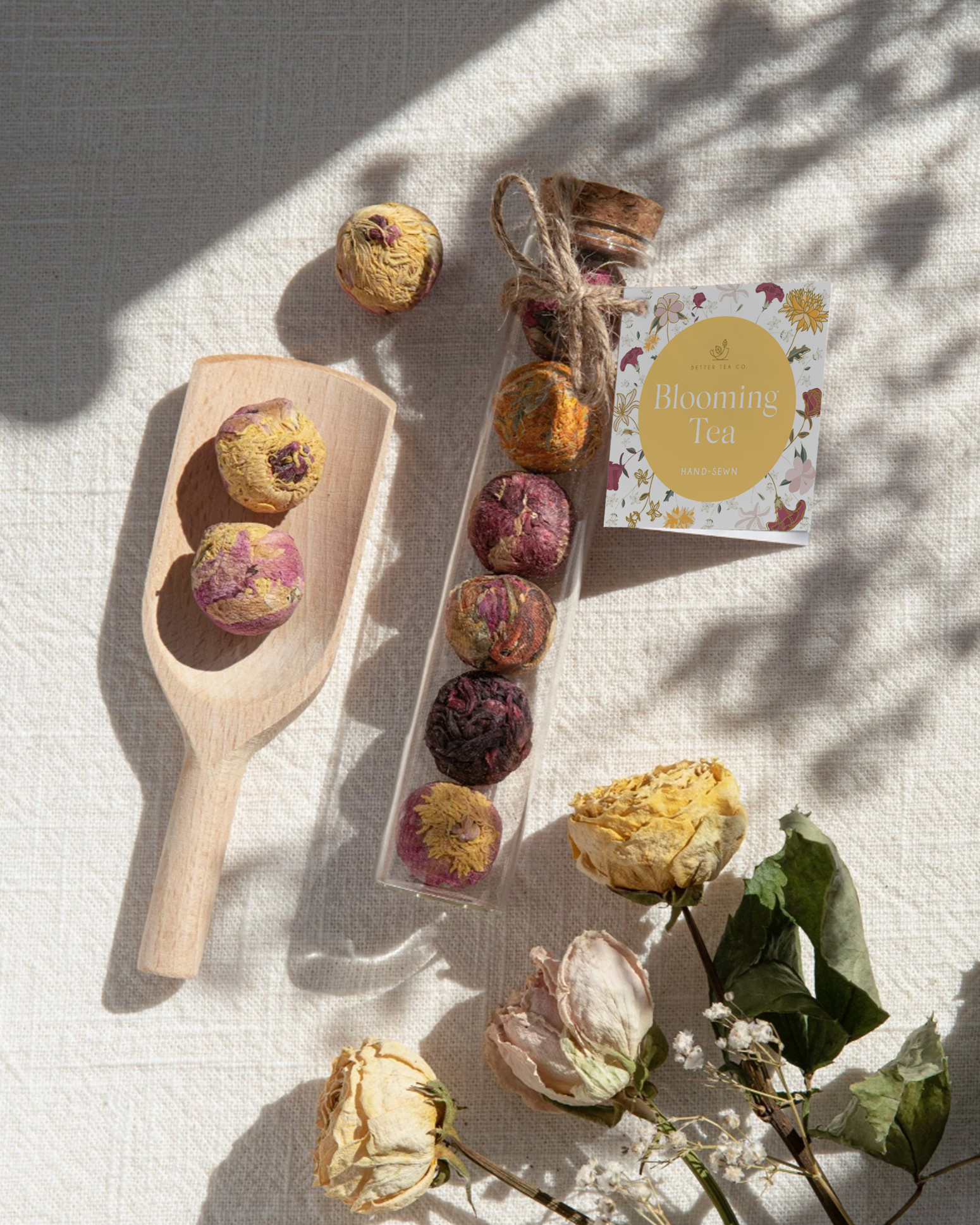 Decorative tea balls, a jar of blooming tea, and dried roses on a light-colored fabric background with shadows.
