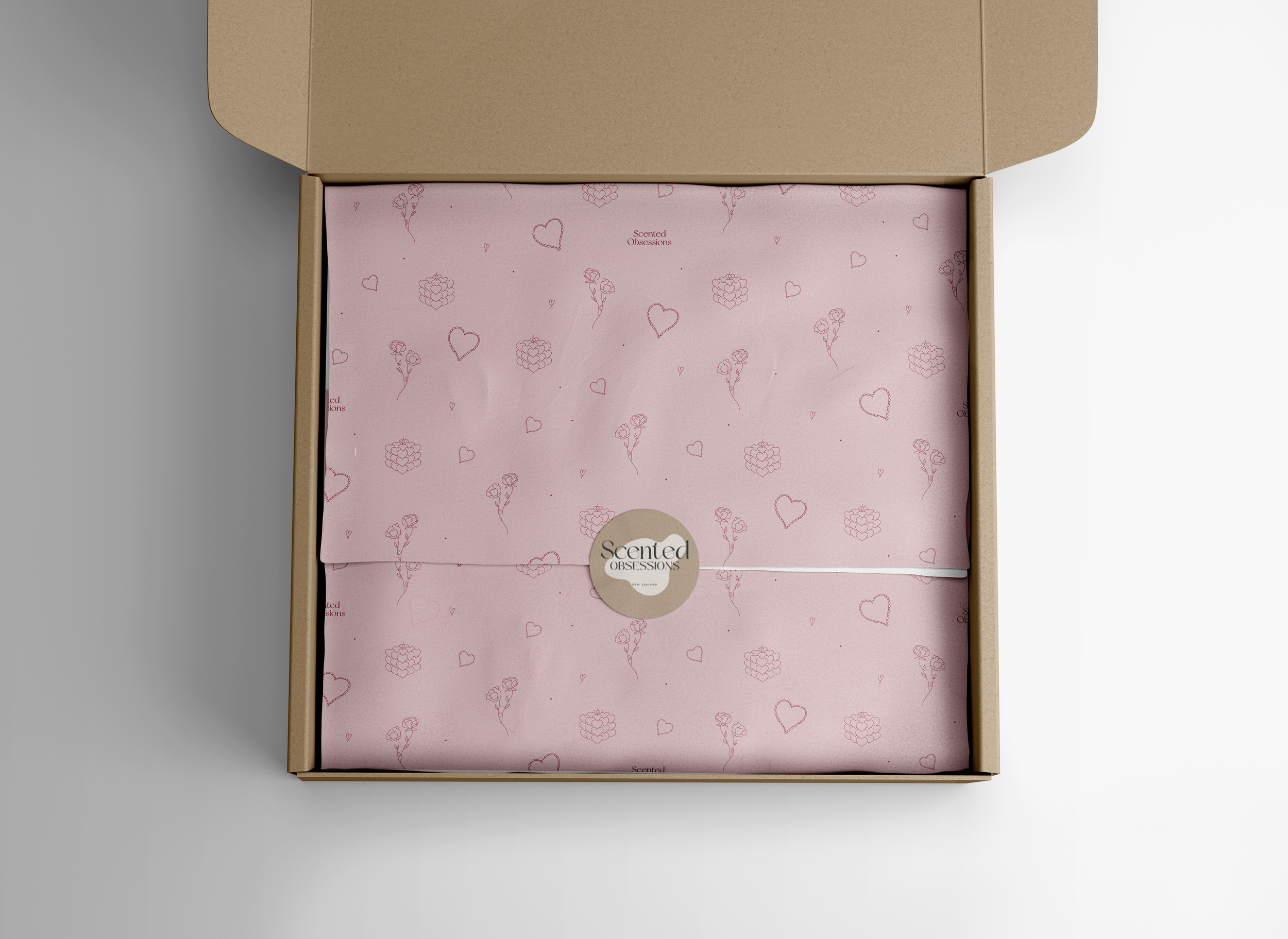 Open cardboard box containing pink tissue paper with Heart, rose, and raspberry patterns, branded with 'Scented Obsessions' logo in the center.