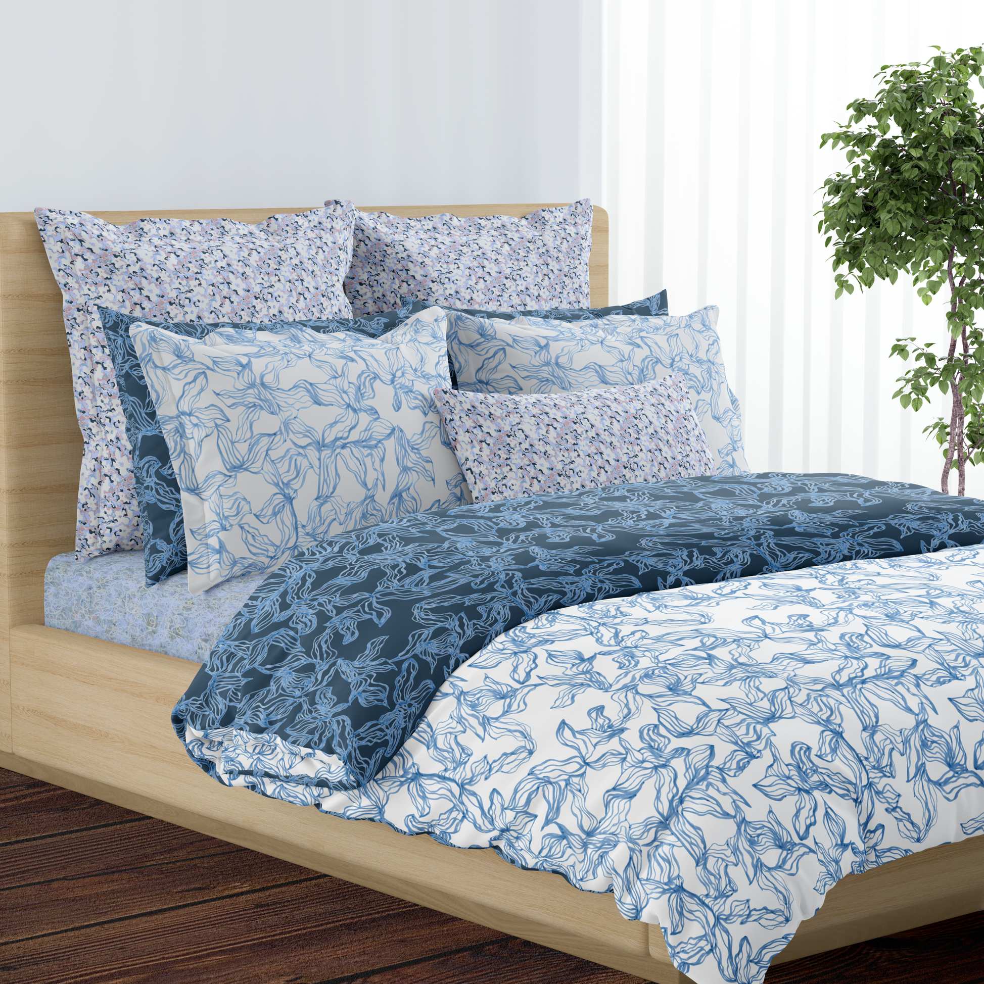 A bed with blue and white floral patterned bedding, surrounded by matching pillows and a wooden headboard, with a potted plant and white curtains in the background.