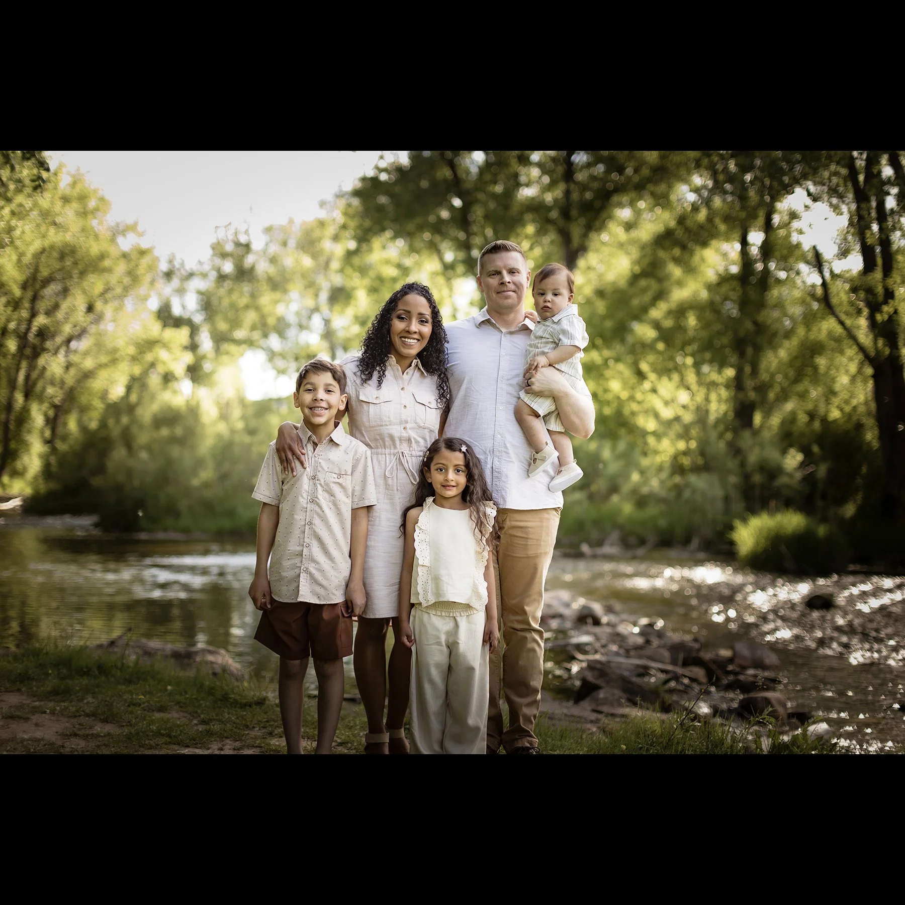 Family of six standing by a river in a lush forest, smiling at the camera.