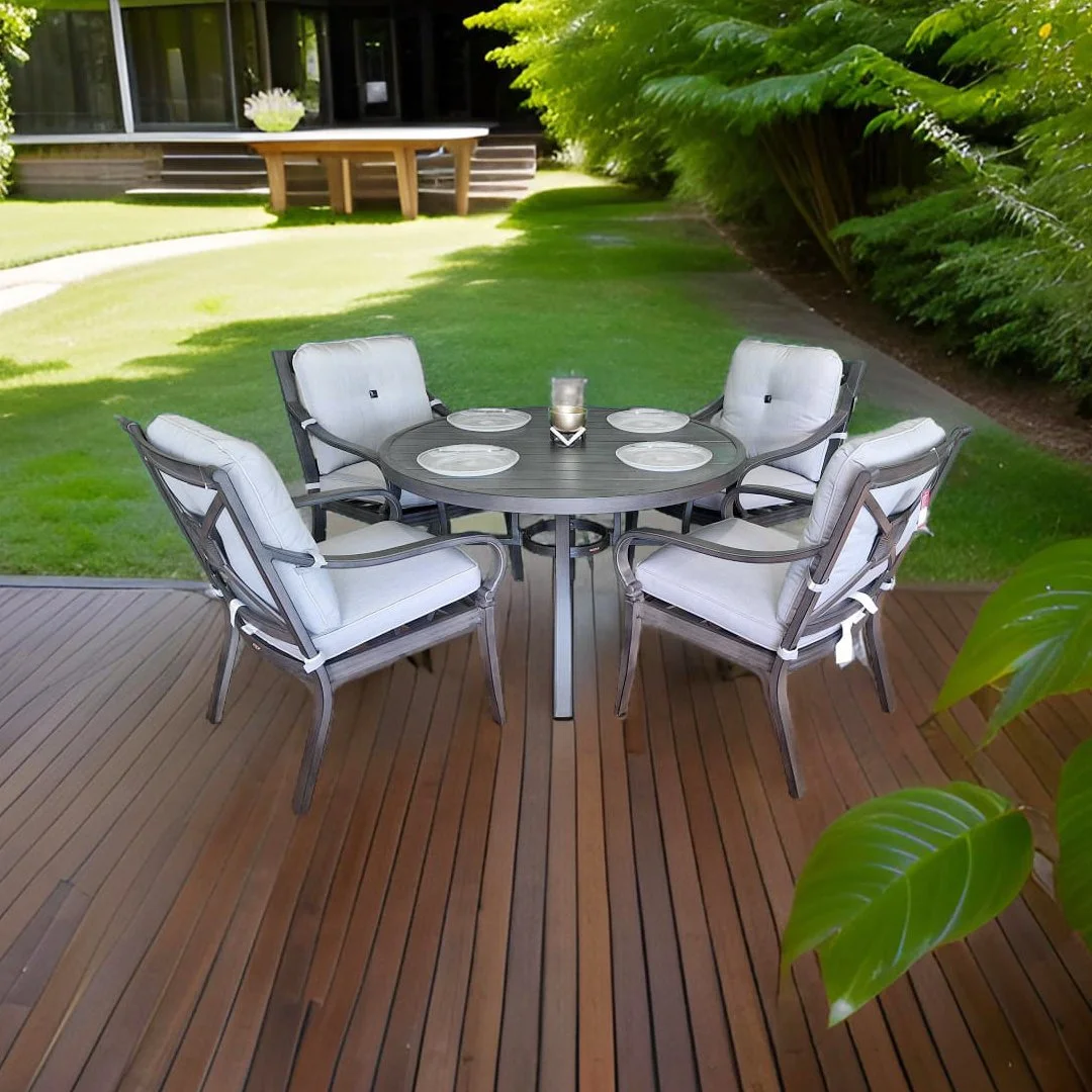 Mesa redonda de estilo moderno en un patio con seis sillas con cojines blancos, sobre una tarima de madera, rodeada de césped y plantas verdes.