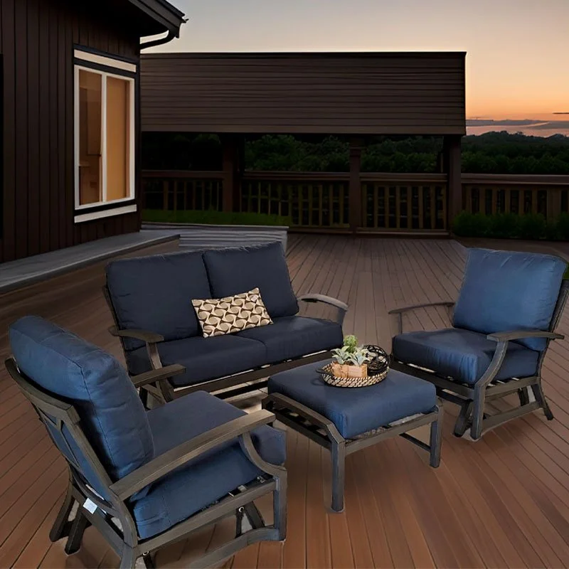 Muebles de terraza con sillas y sillón con cojines azules, una mesa pequeña con decoraciones, en un balcón de madera al atardecer.