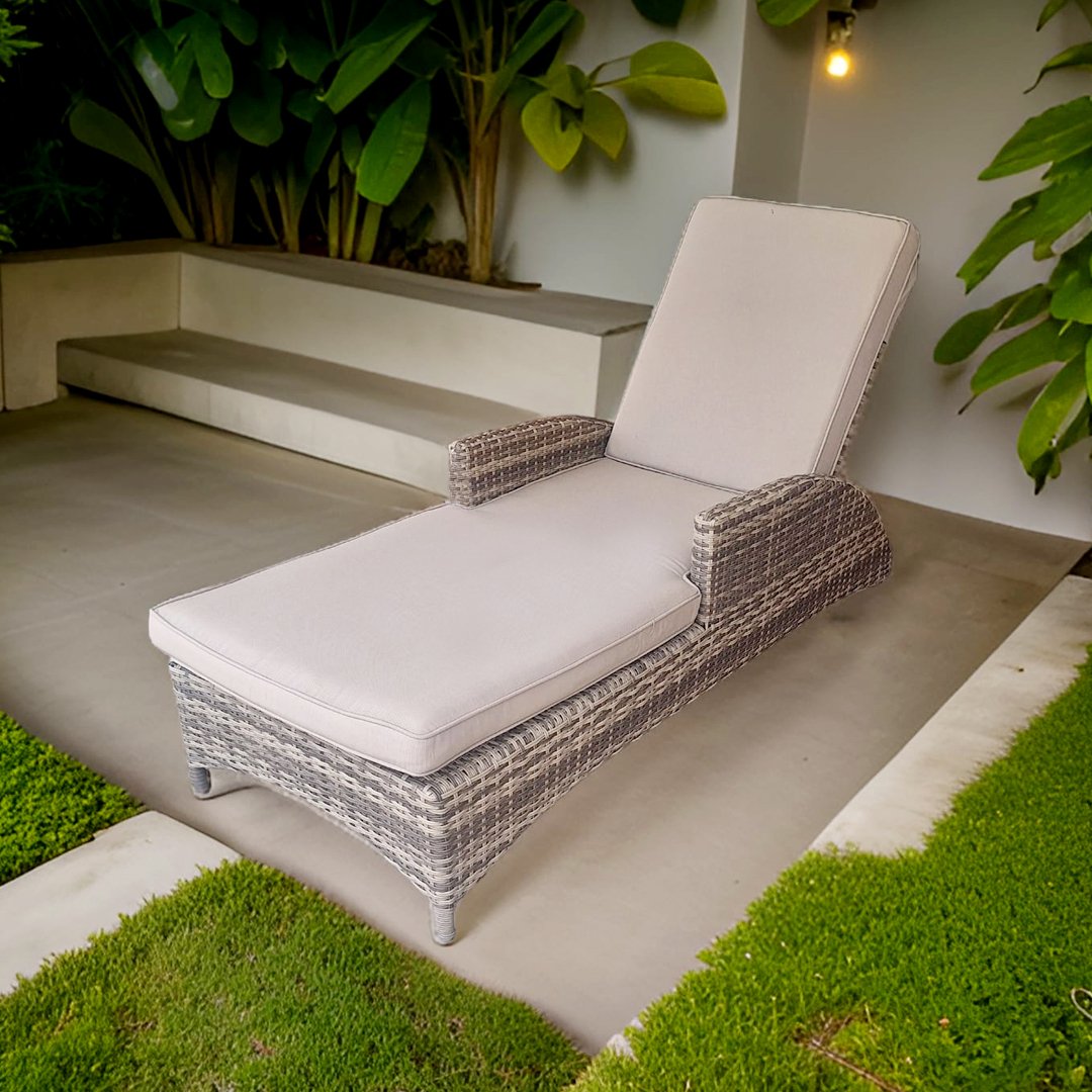 Una tumbona de mimbre con cojines beige en una terraza con plantas verdes y césped