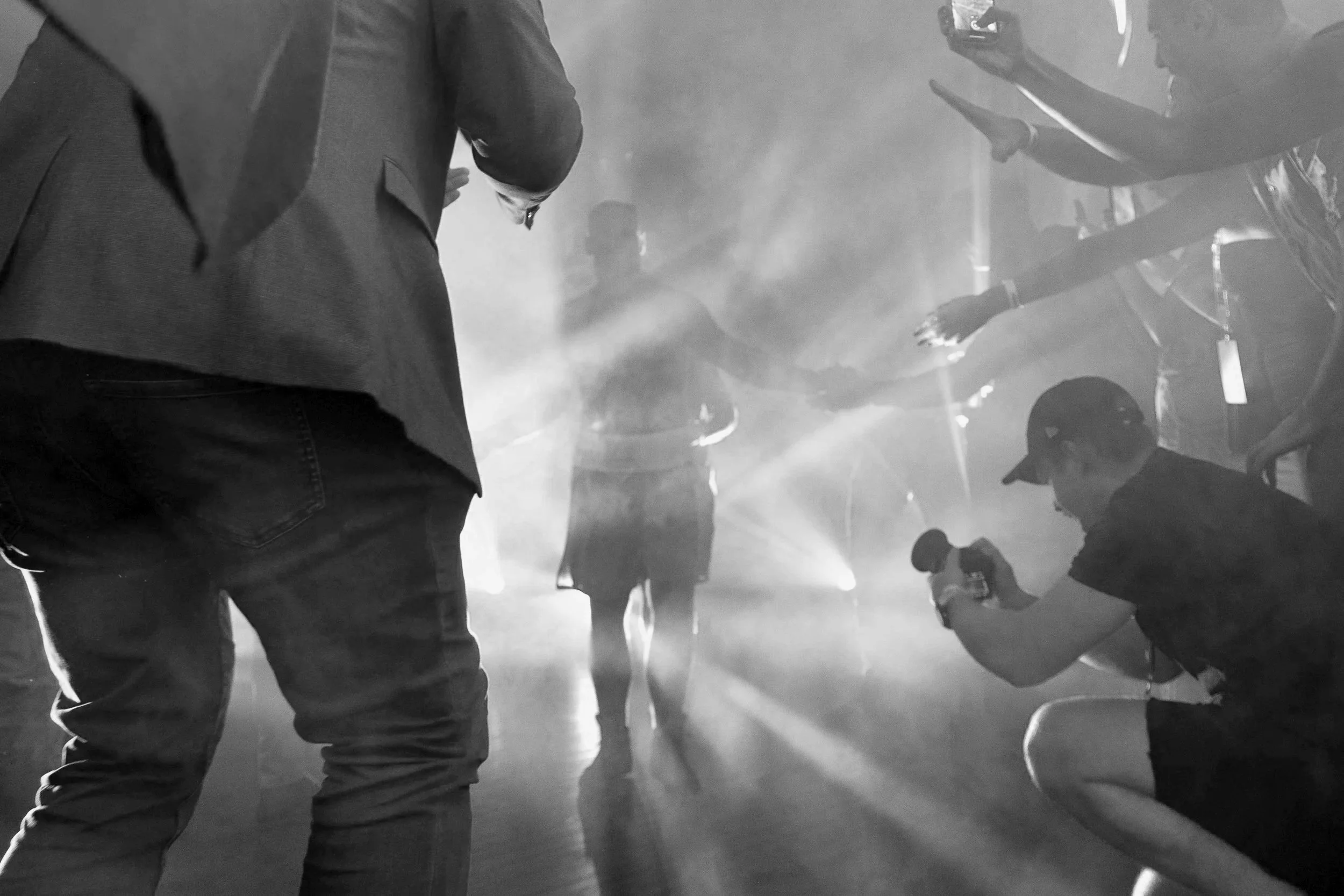 Black and white photo of people dancing in a smoky nightclub with beams of light shining through.