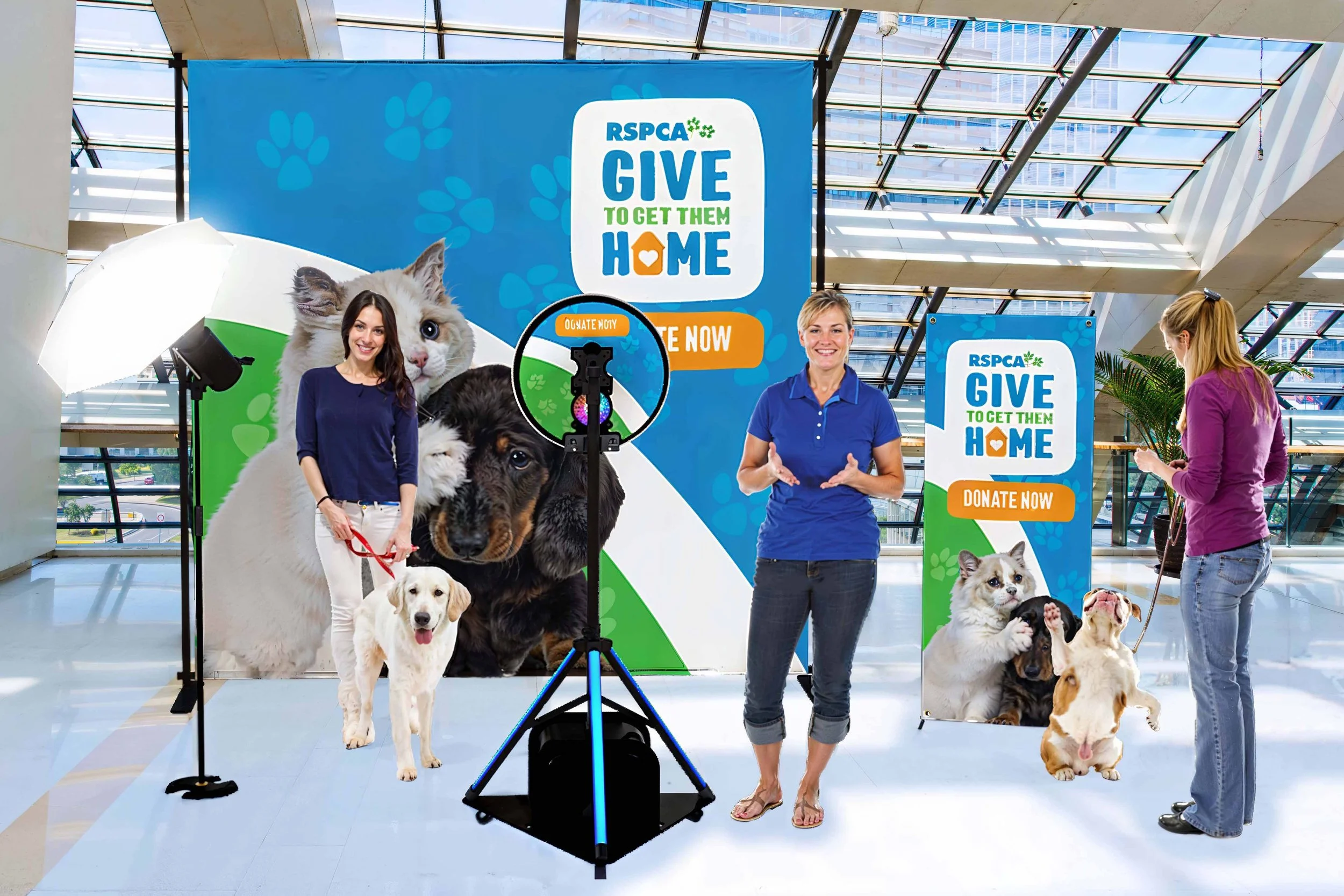 Professional photography of a Darwin RSPCA pet adoption event at a modern indoor venue, featuring 'Give to Get Them Home' campaign banners and happy pet owners.