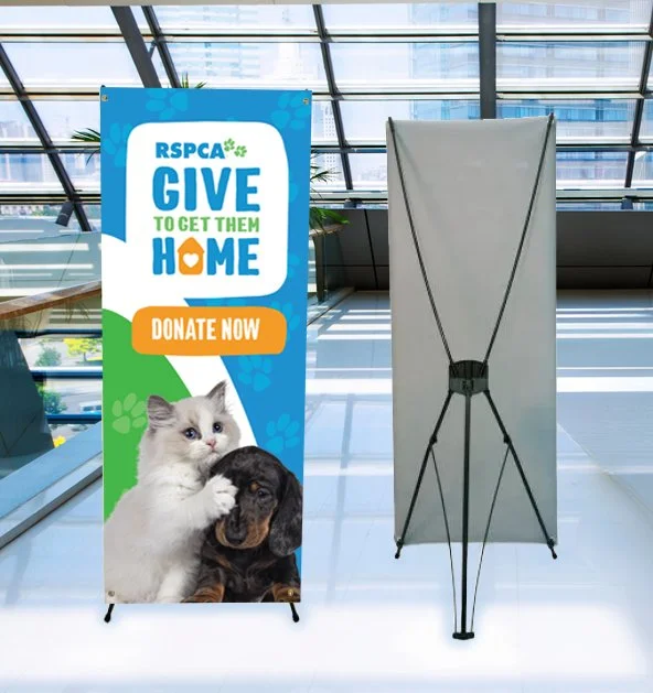 RSPCA 'Give to Get Them Home' pull-up banner by Ausome Love Studio with kitten and puppy imagery and QR code for donations in a large event hall.