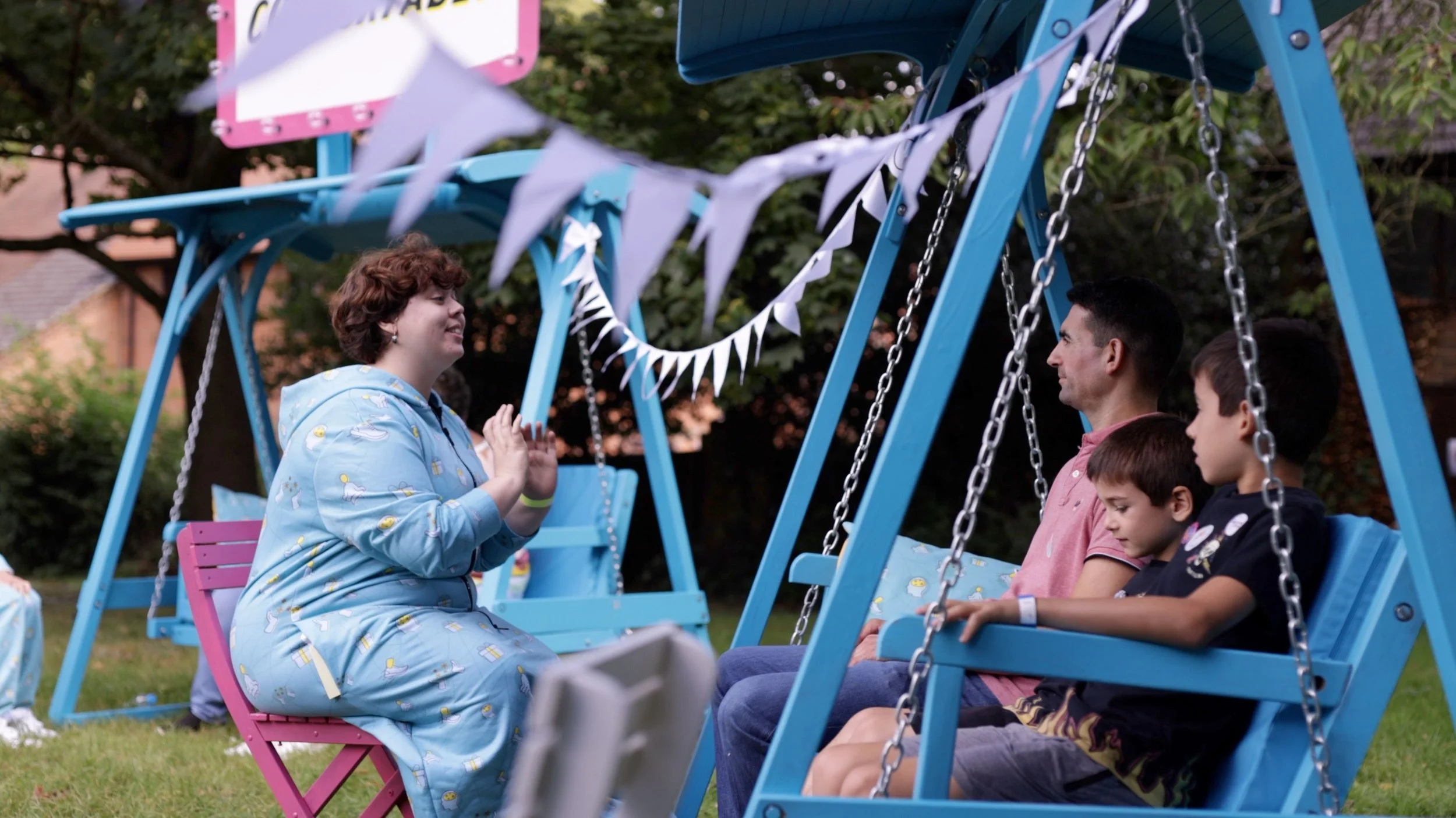 People sitting on blue swings outdoors at a Take Ten event hosted by Fluid Motion Theatre