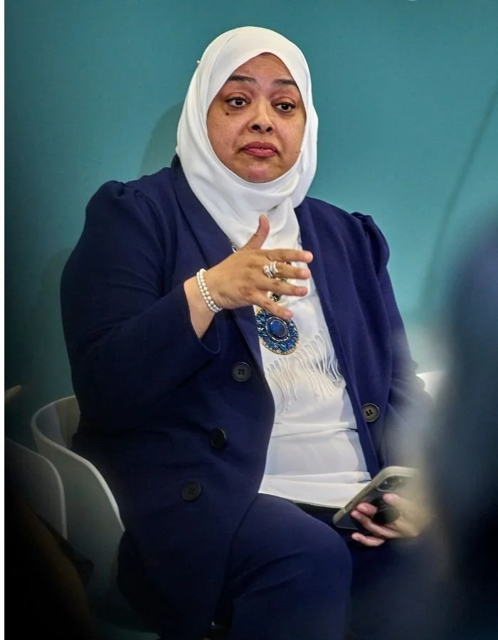 Nurjahan Khatun, coach & speaker.  a white hijab and a blue blazer sitting and gesturing with her hand.