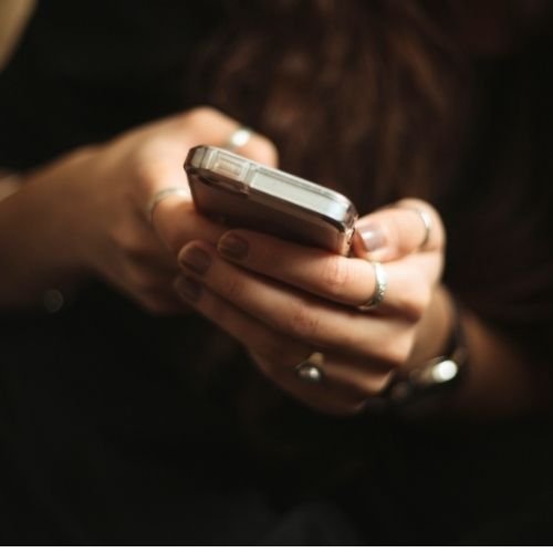 Close-up of a person holding a smartphone with both hands, fingers visible, wearing rings.