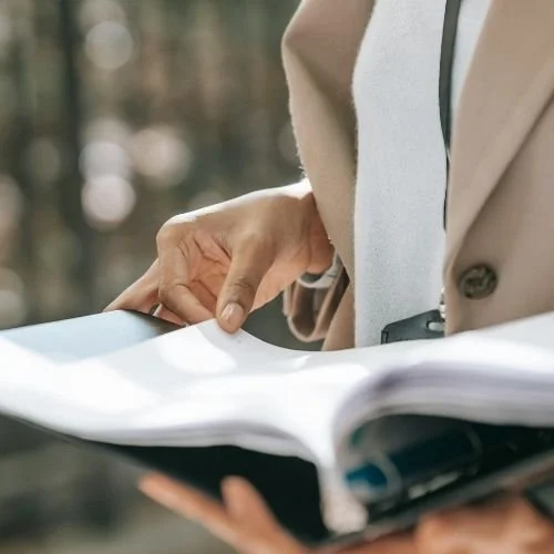 Close-up of a person holding an open book outdoor of an office building. Nurjahan Khatun, coach & speaker.