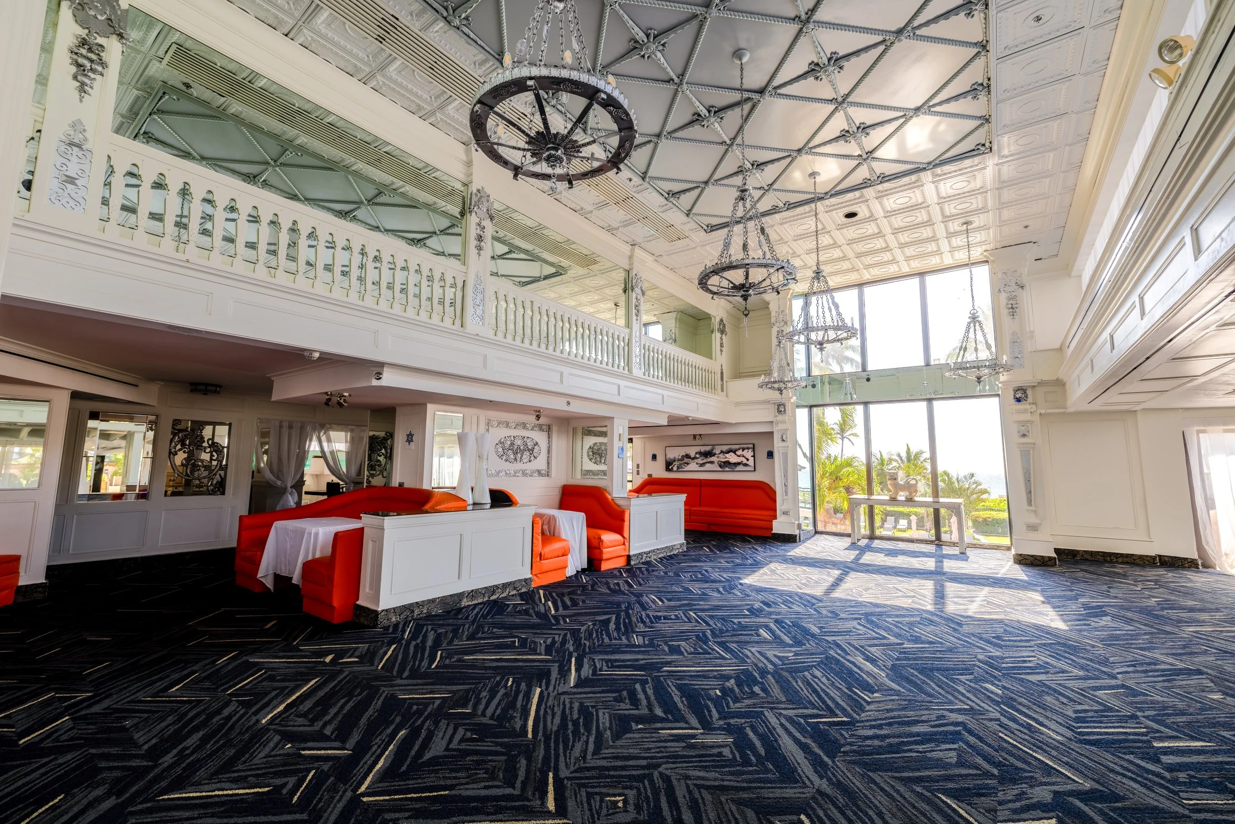 Elegant interior of a hotel lobby with white walls, ornate chandeliers, orange seating, and patterned carpet.