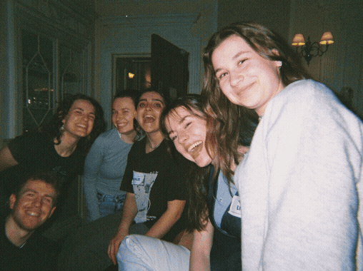 Five women and one man smiling and posing together indoors at a social gathering.