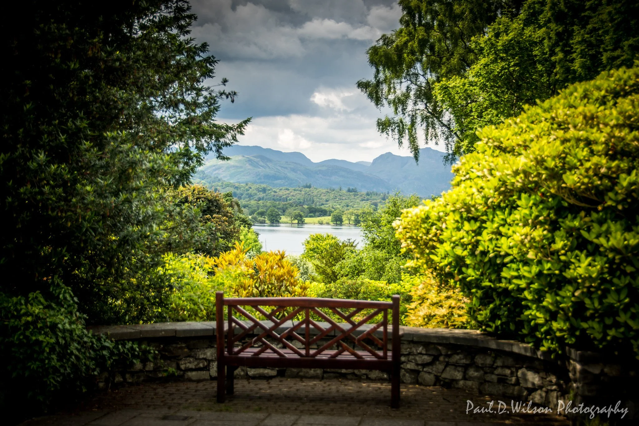 bench overlooking a lakem mountains and lots of trees creating a frame around the image