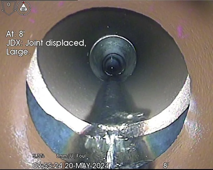 View inside a pipeline showing a displaced joint, with inspection data overlaid. The image captures the pipe's interior from a camera, indicating the joint is large and dislocated. Details include the location at 8 feet, date May 20, 2024, and time 09:55.