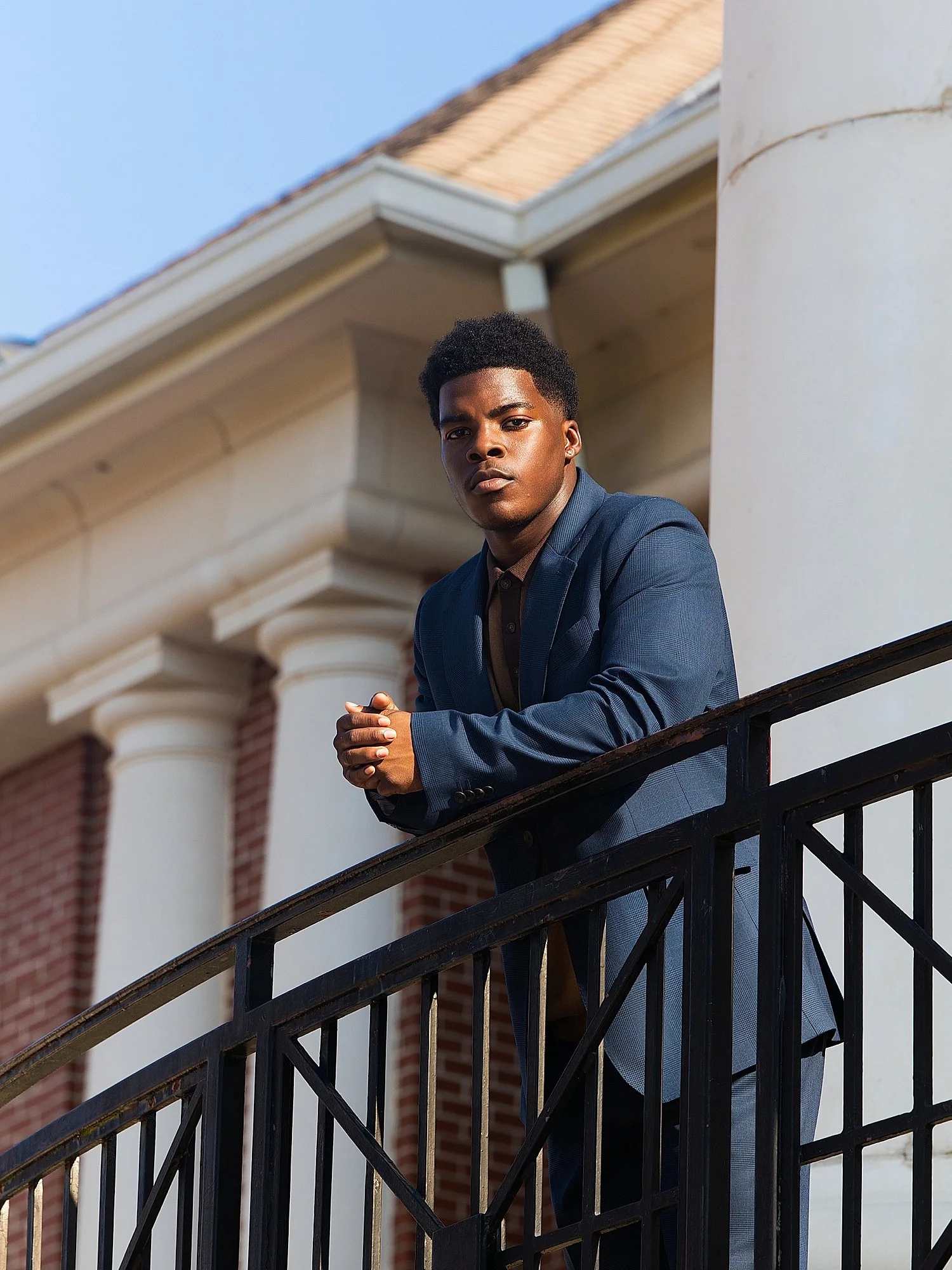black man leans over balcony railing for senior portraits