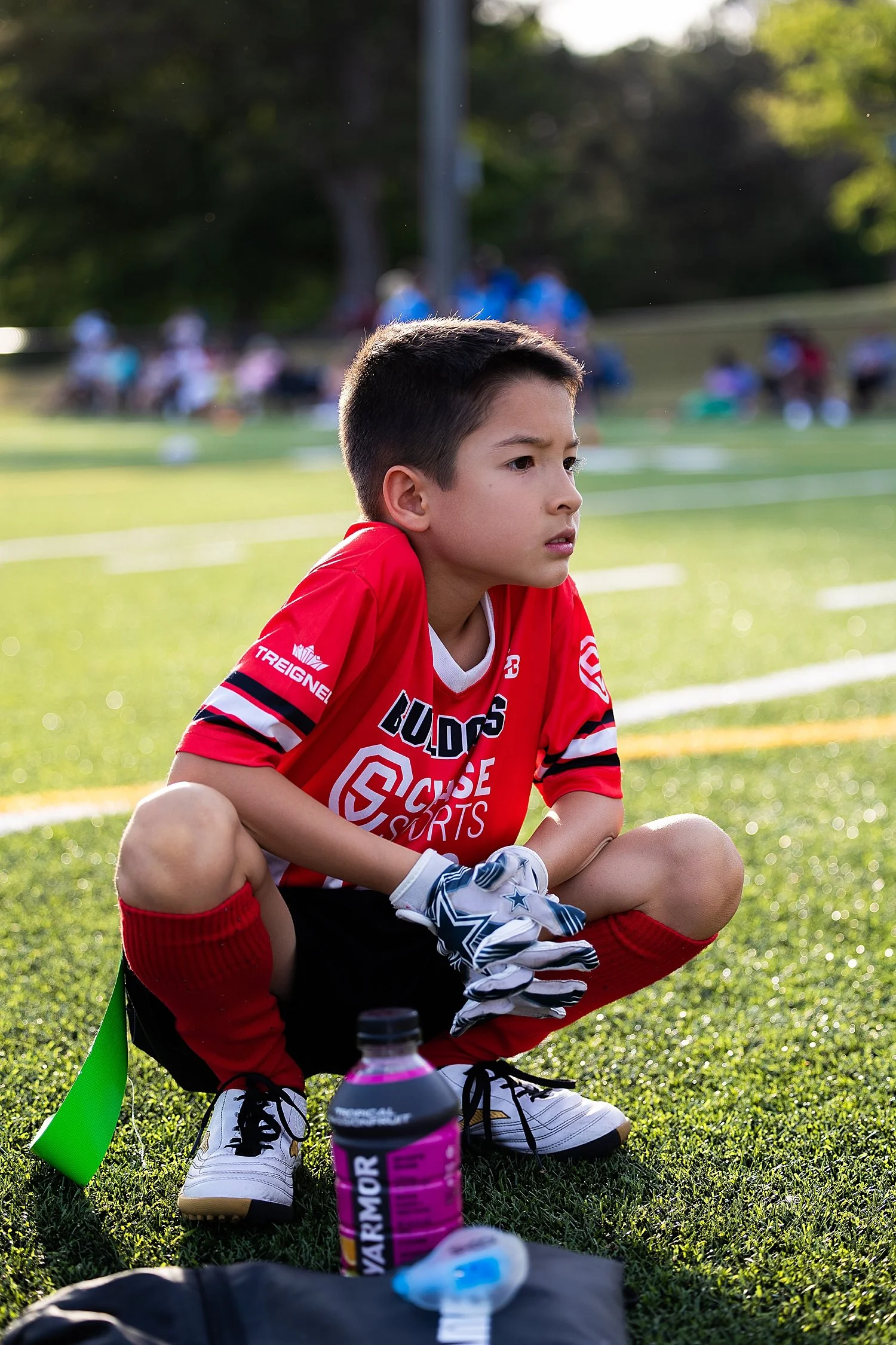 young athlete in red uniform kneels on field by Tiaras Monet Photography