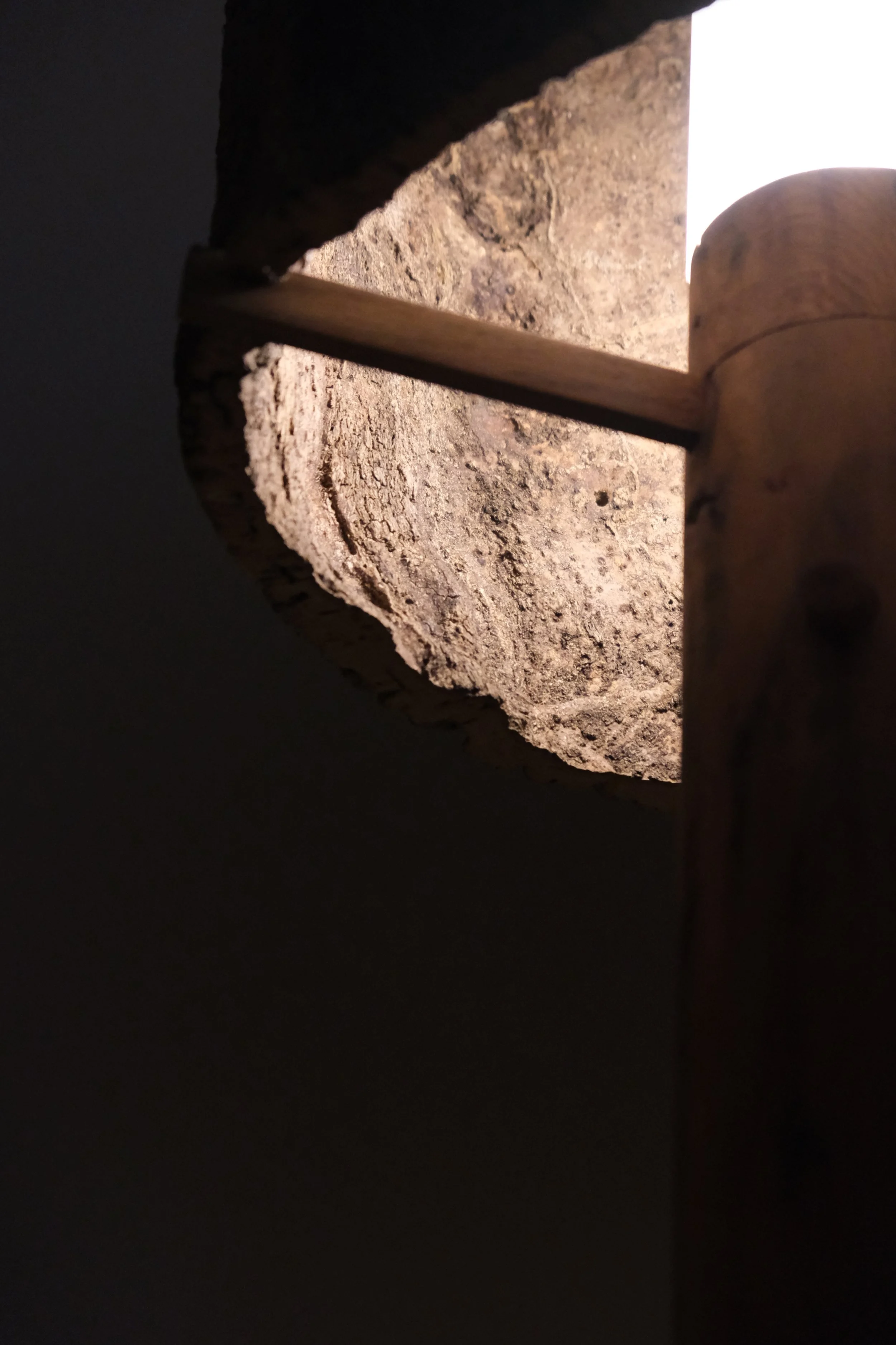 Looking up through a rectangular opening in a stone wall, with a wooden beam and part of a wooden stick visible.