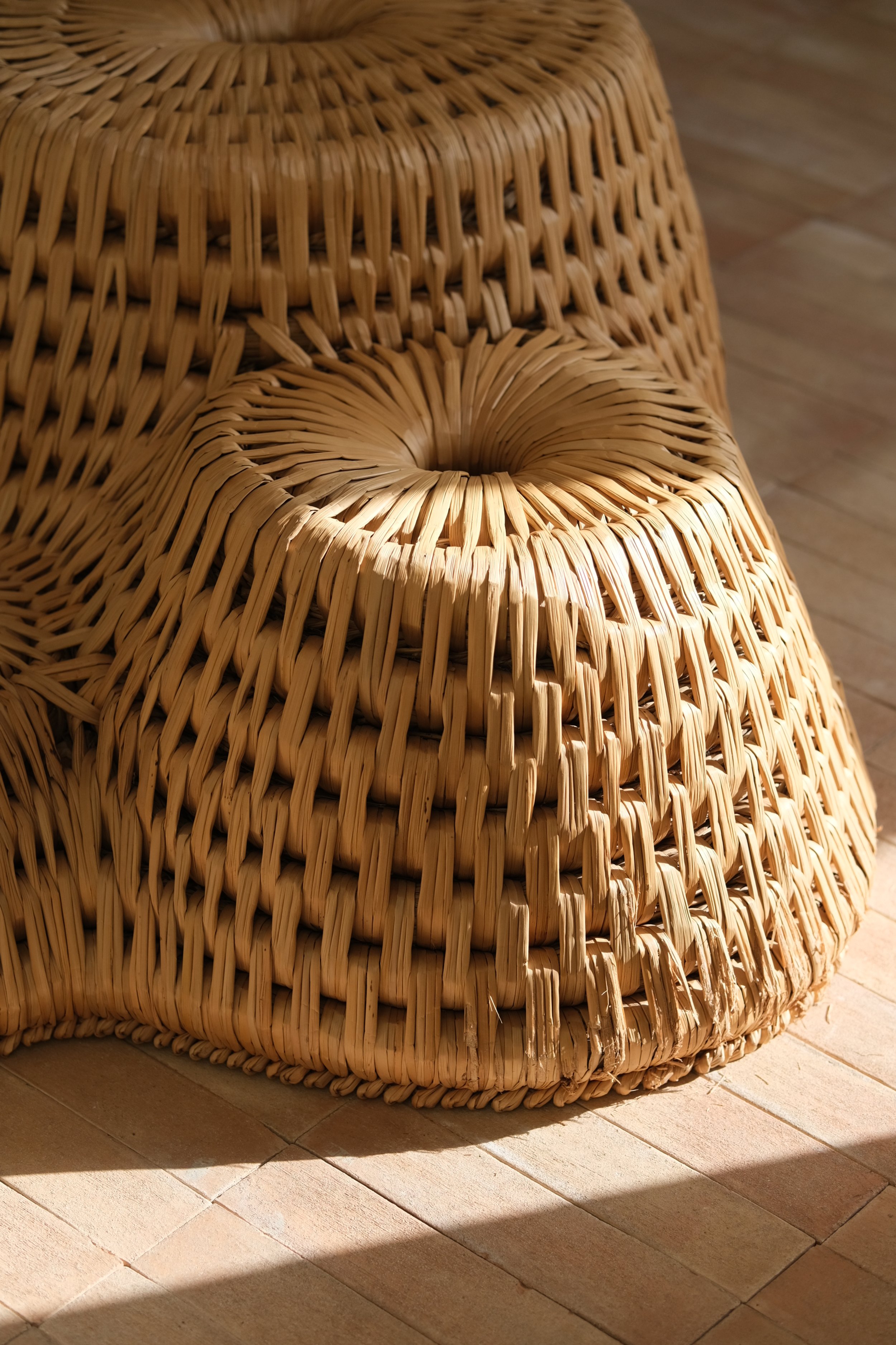 Stacked woven rattan stools on a tile floor with sunlight casting shadows.