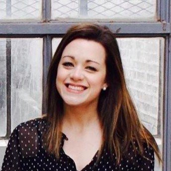 A woman with long brown hair smiling in front of a window.