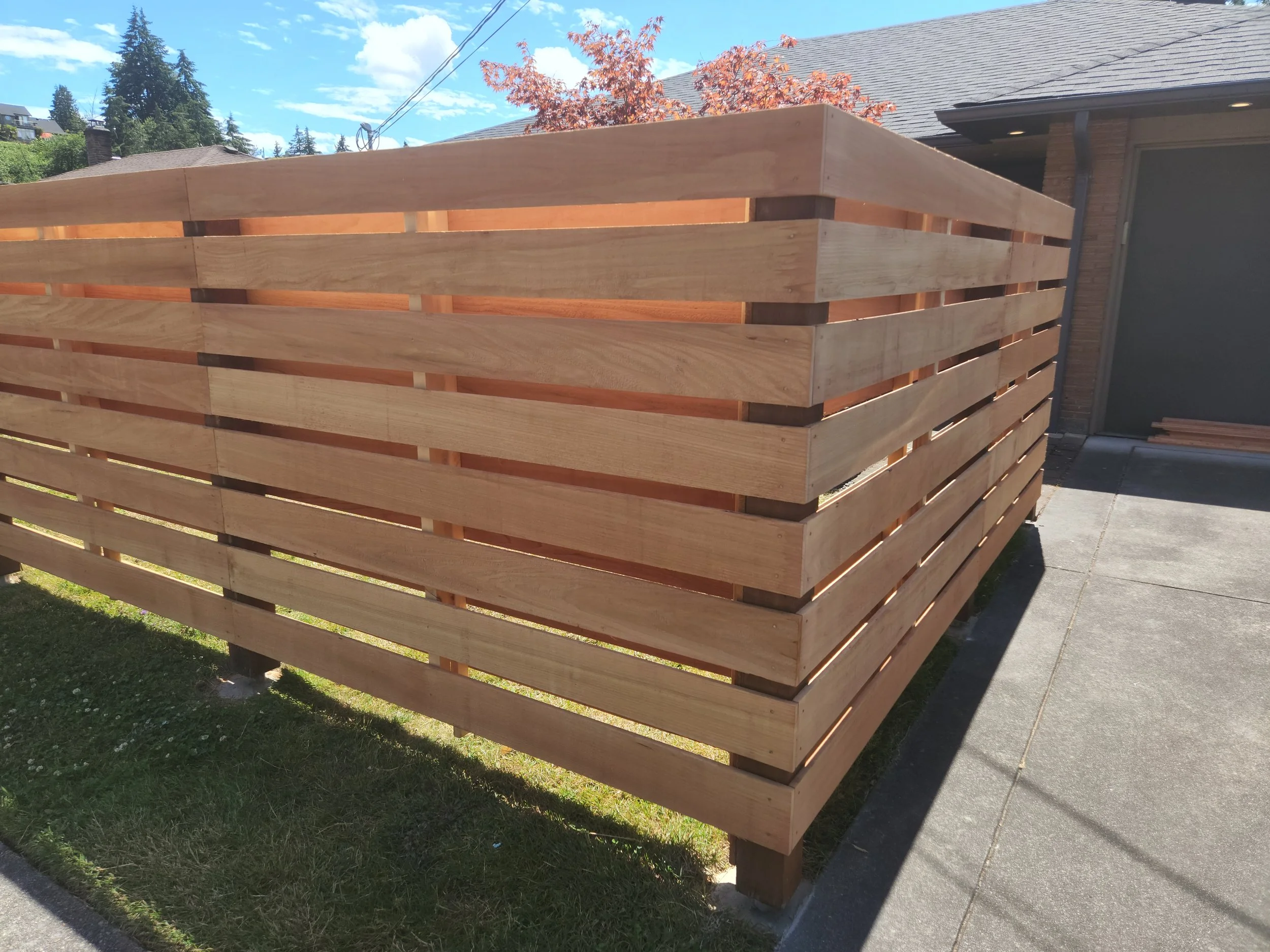 A wooden slat privacy fence built on a front lawn in a residential neighborhood.