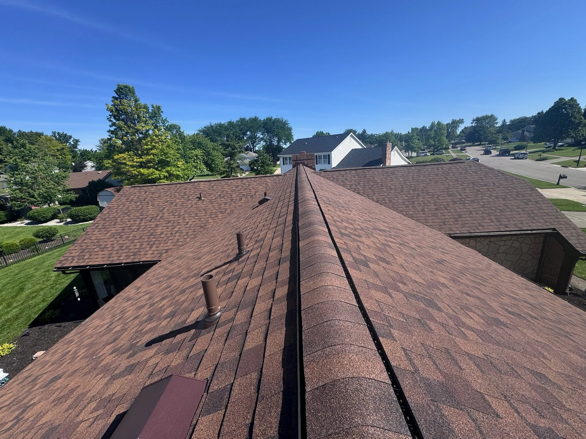 View of rooftops and suburban neighborhood with trees under a clear blue sky.