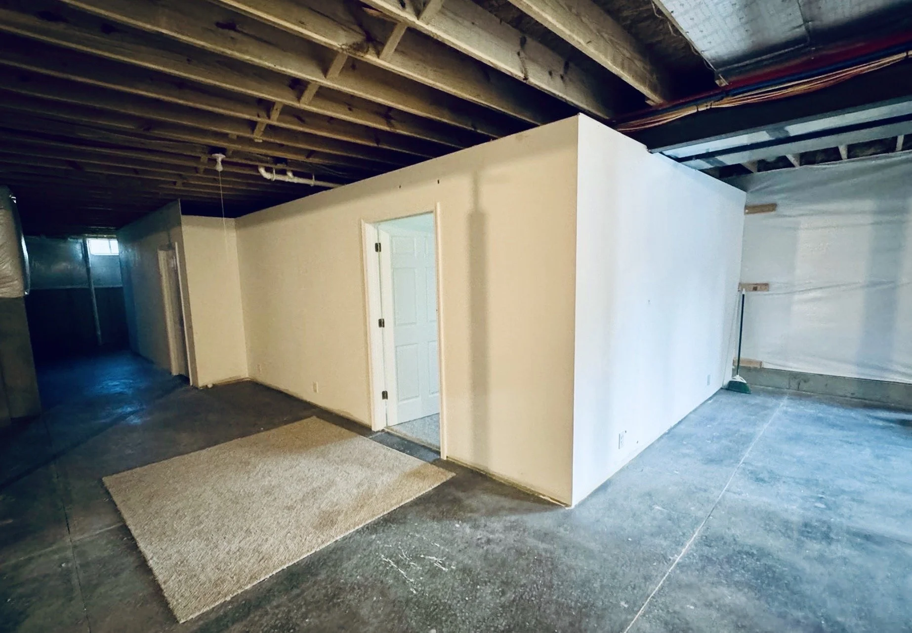 Interior of a basement with exposed wooden ceiling beams, a small beige carpet, white walls,