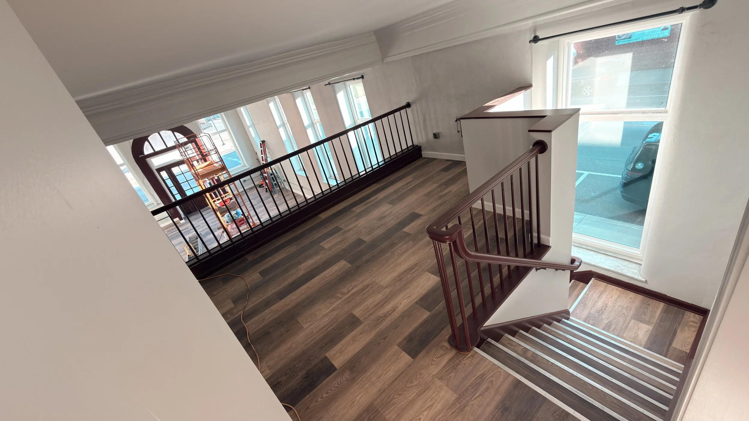 View of a stairway landing with wooden flooring, a dark wooden handrail, and a large window letting in natural light, overlooking a parking lot with cars.
