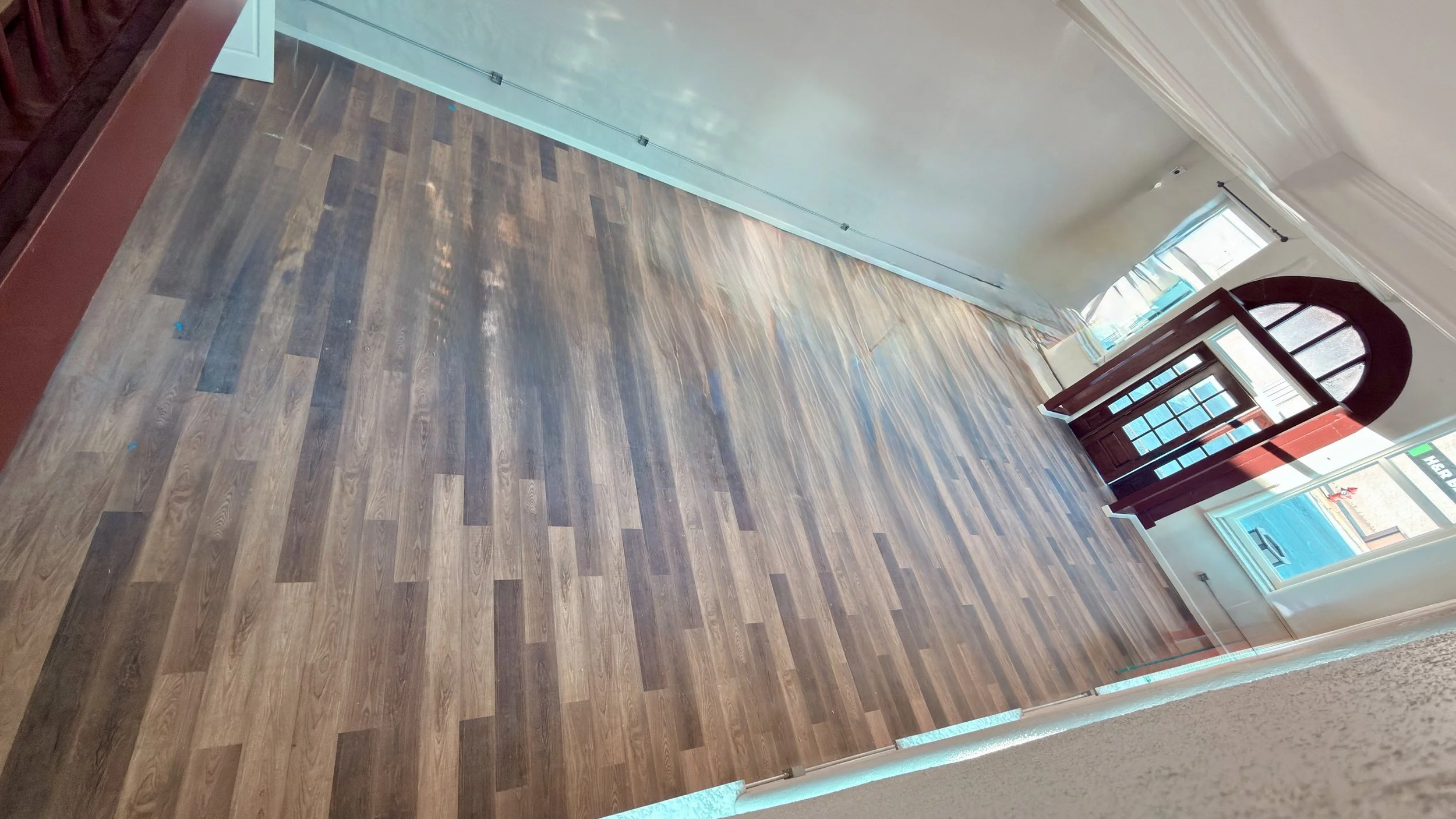 Interior of an empty room with hardwood flooring, large window, and an open door leading outside.