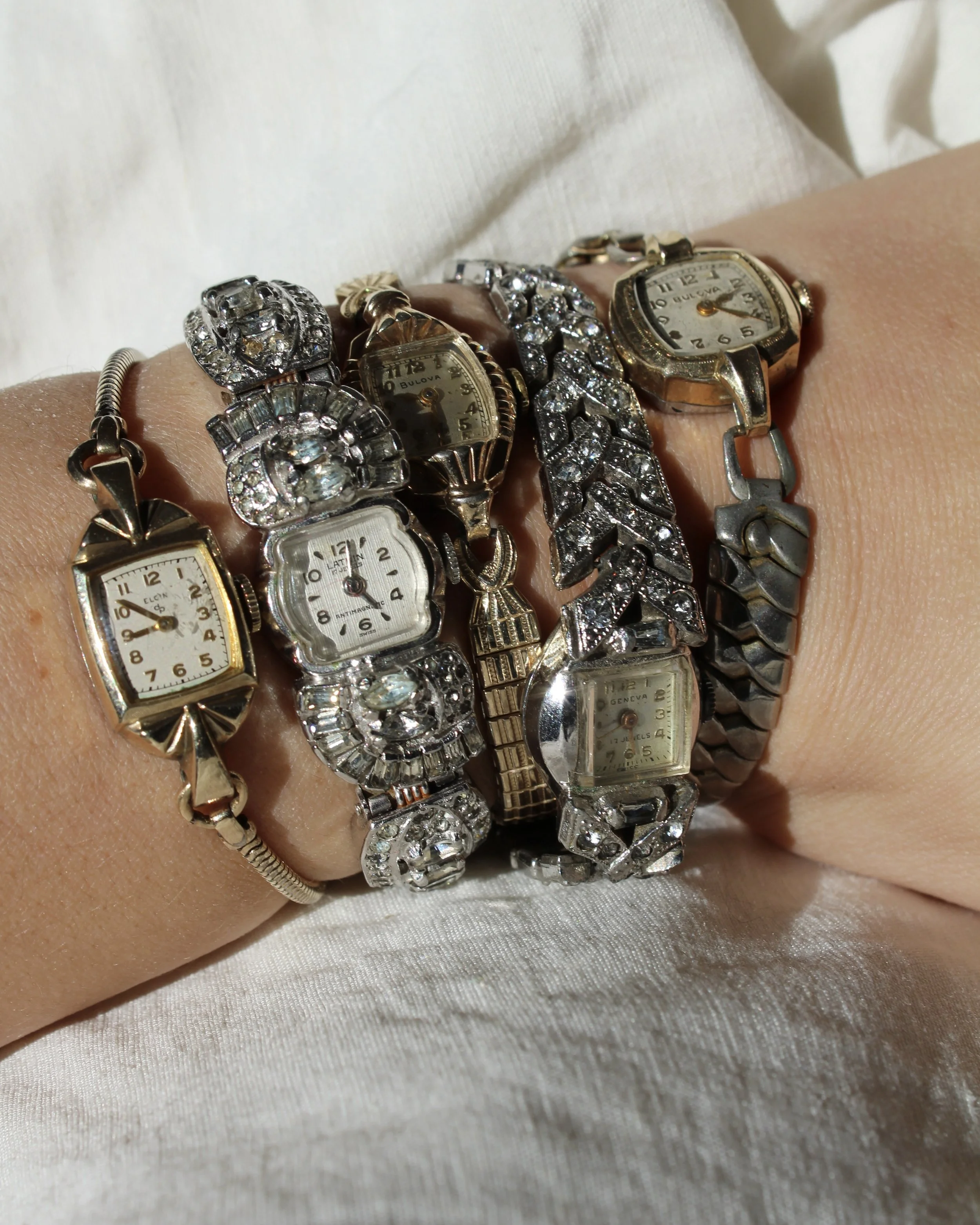 Multiple vintage wristwatches with metallic and jeweled bands on a person's wrist.