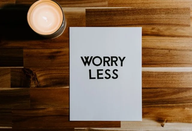 A piece of paper with the words “worry less” on a wooden table, next to a candle.