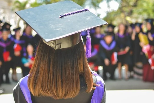 A woman in university garb and a graduation hat, with long hair.