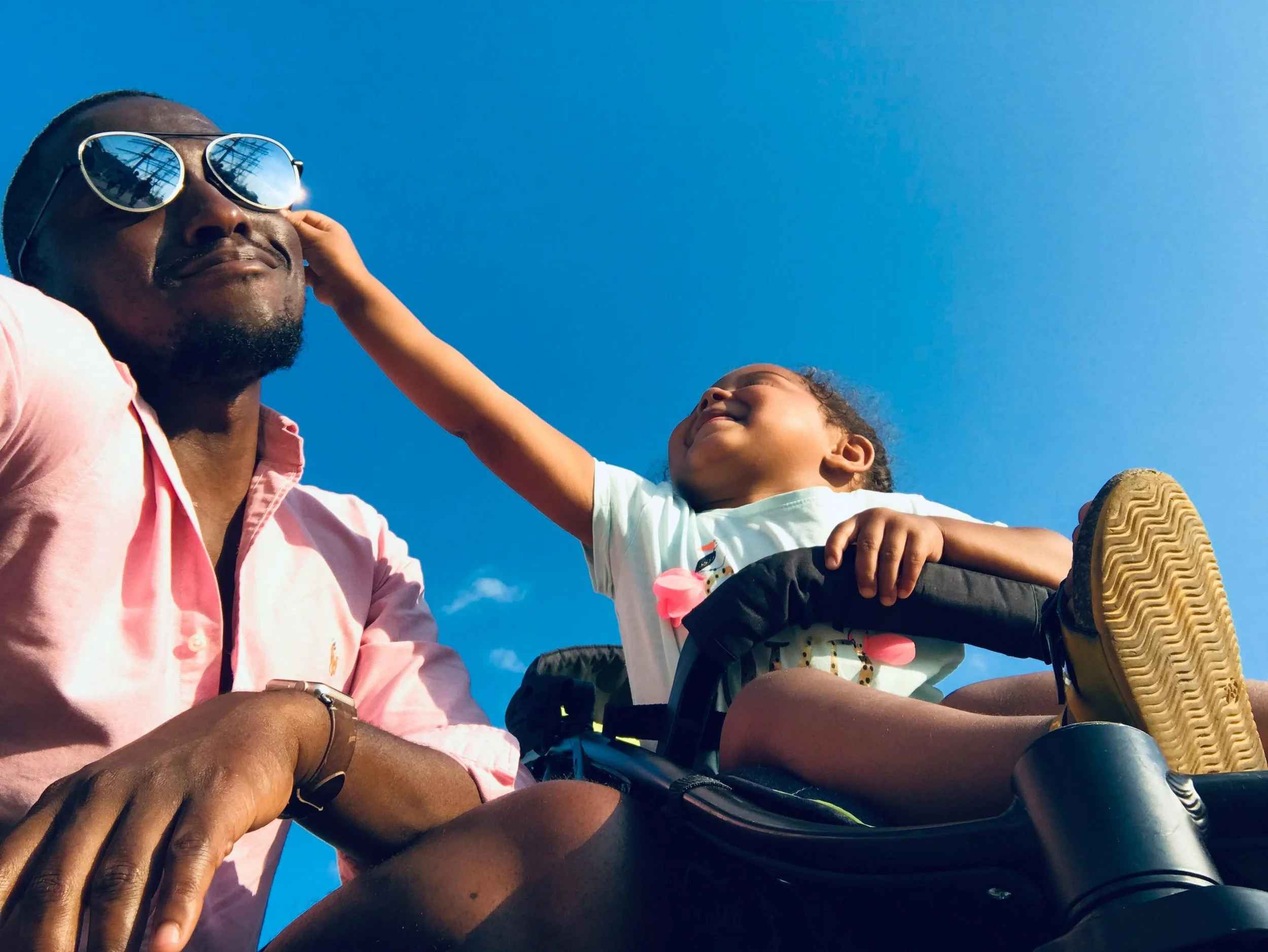 A young toddler child grabbing playfully onto her Father's sunglasses