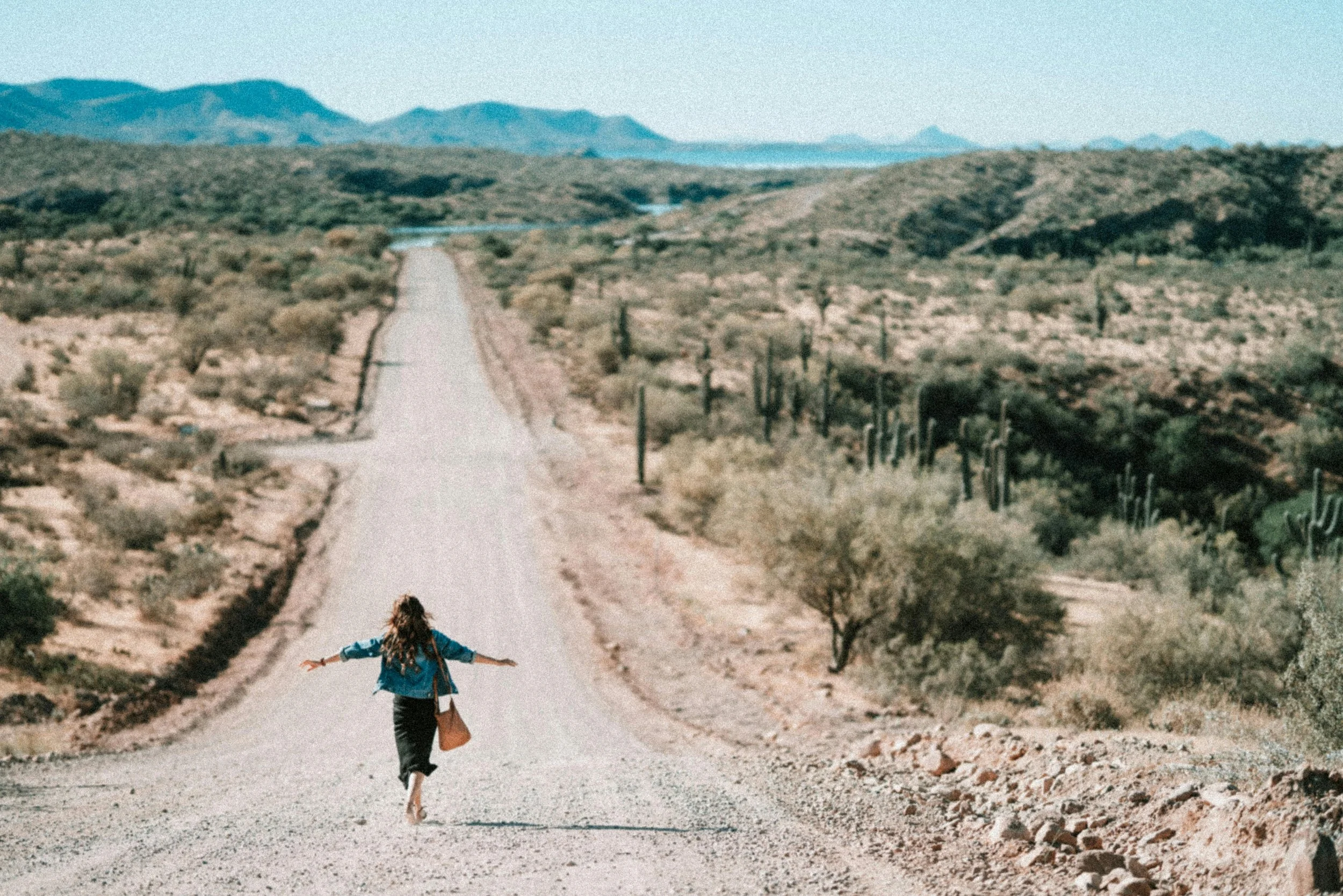A woman walking toward and into the desert on a road with cacti