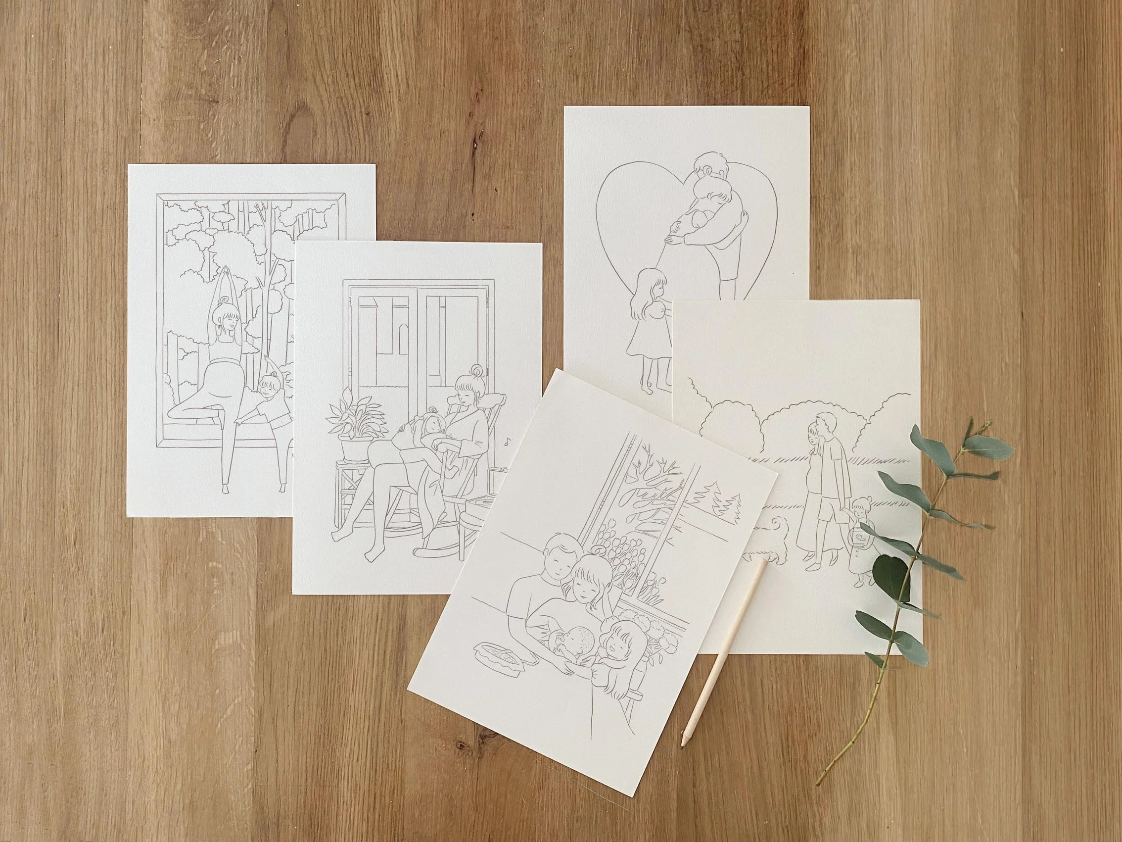 A wooden table with five paper sketches of people and nature scenes, a white pencil, and a sprig of green leaves.