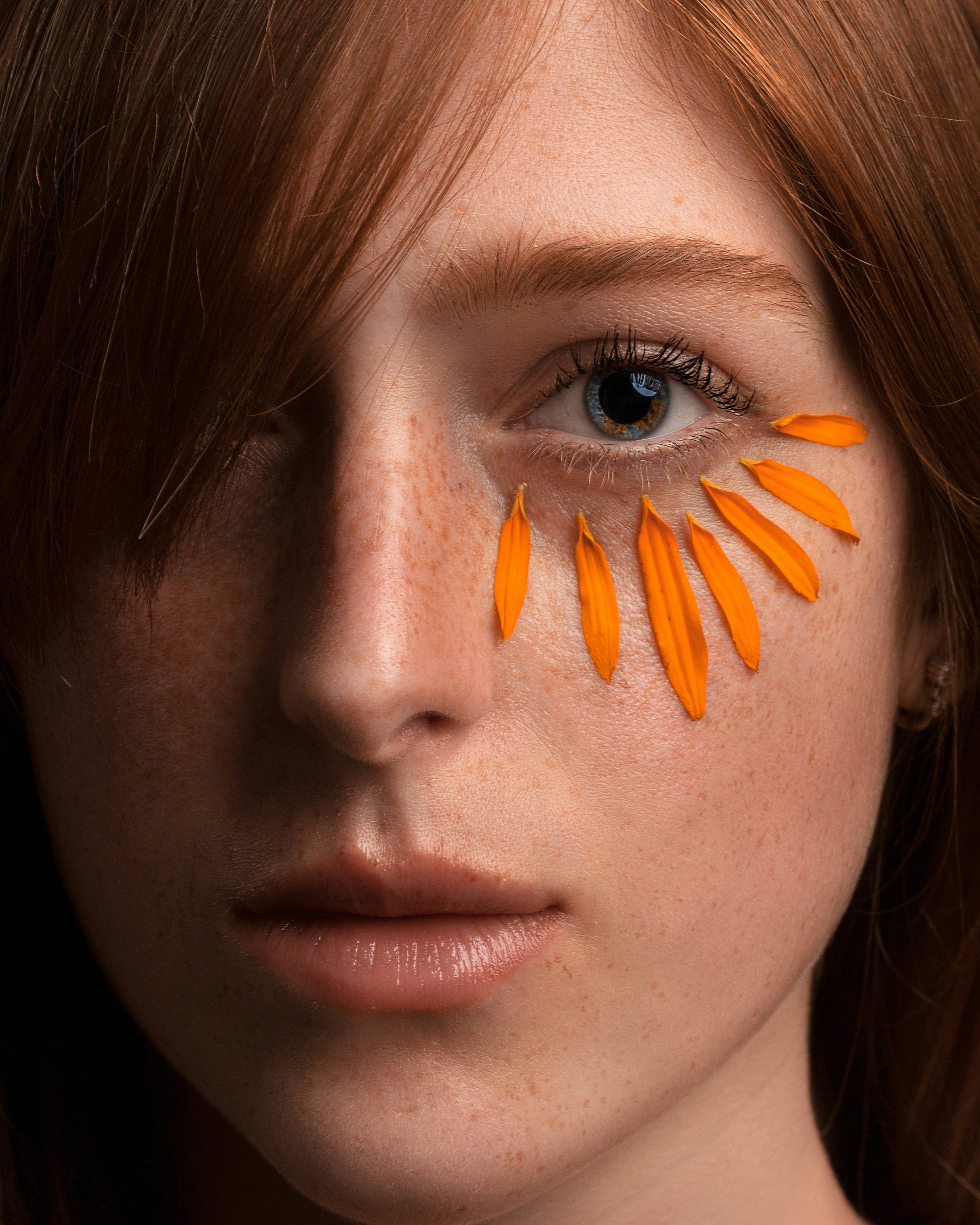Girl with blue eyes and red hair looking at camera- she has marigold peteals around the base or lower part of her eye socket looking like massive eyelashes, I am using them to denote eye strain for the blog