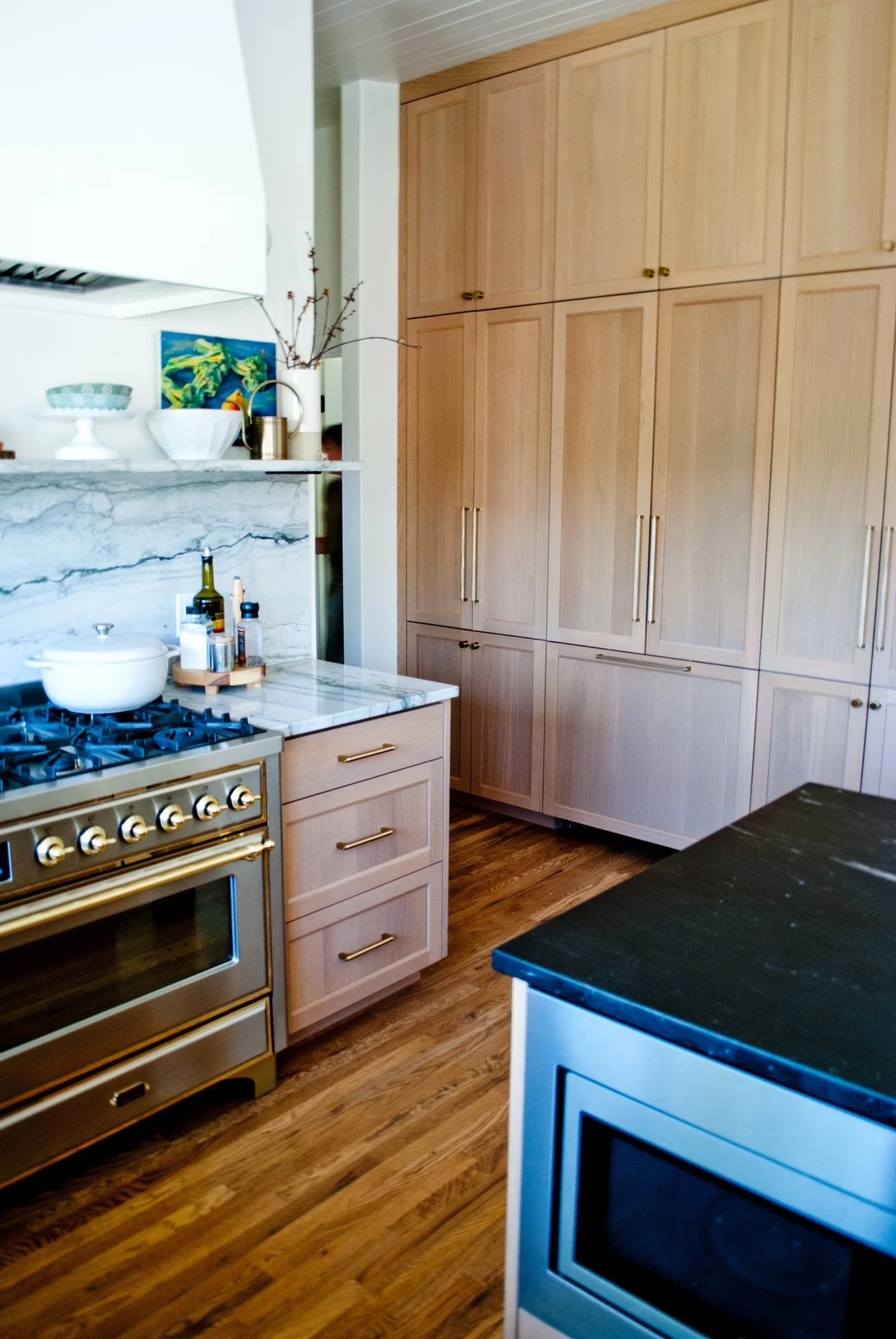 A modern kitchen with wooden cabinets, a marble countertop, a stainless steel oven, and a black granite kitchen island.