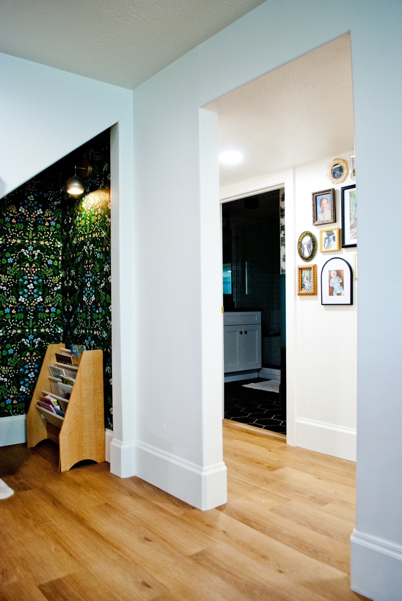 A hallway with a partial view of an adjacent room displaying a wall of family photos and a black-painted room with white furniture.