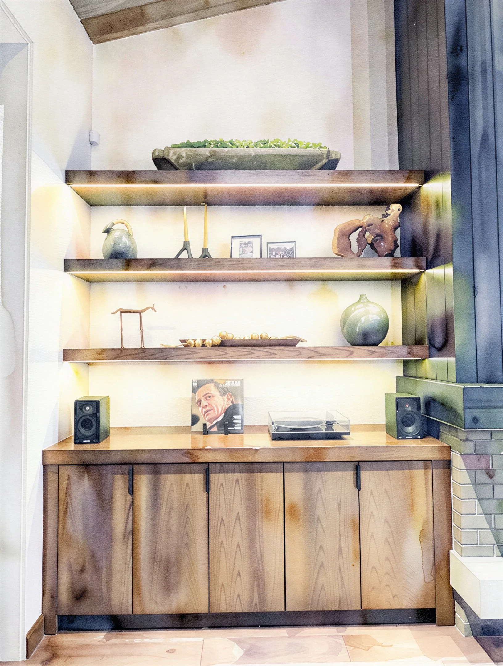 Wooden cabinet with shelves holding decorative items, a vinyl record player, and a framed picture of a man, with black speakers on either side.