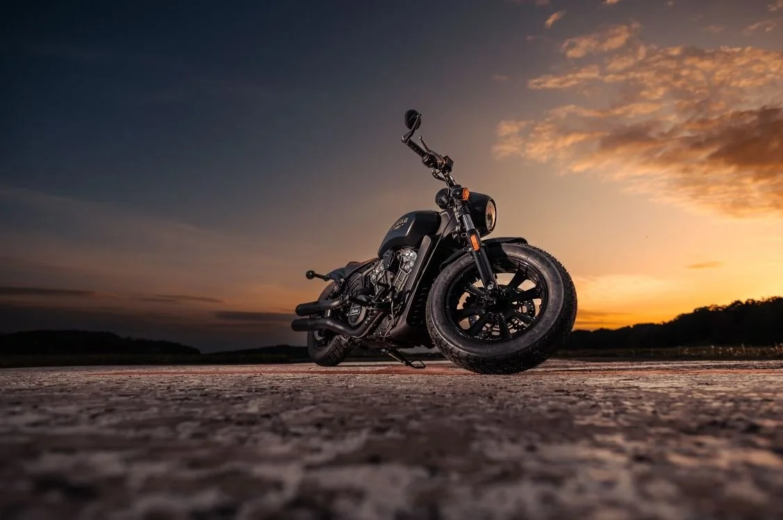 Black motorcycle parked on a flat surface at sunset with a colorful sky.