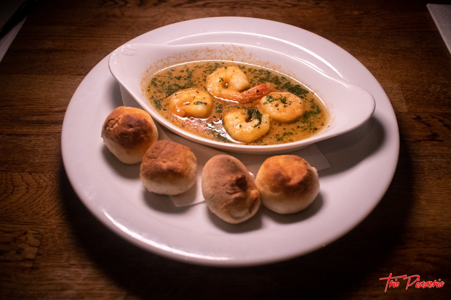 Shrimp in garlic butter sauce with bread rolls on a white plate.
